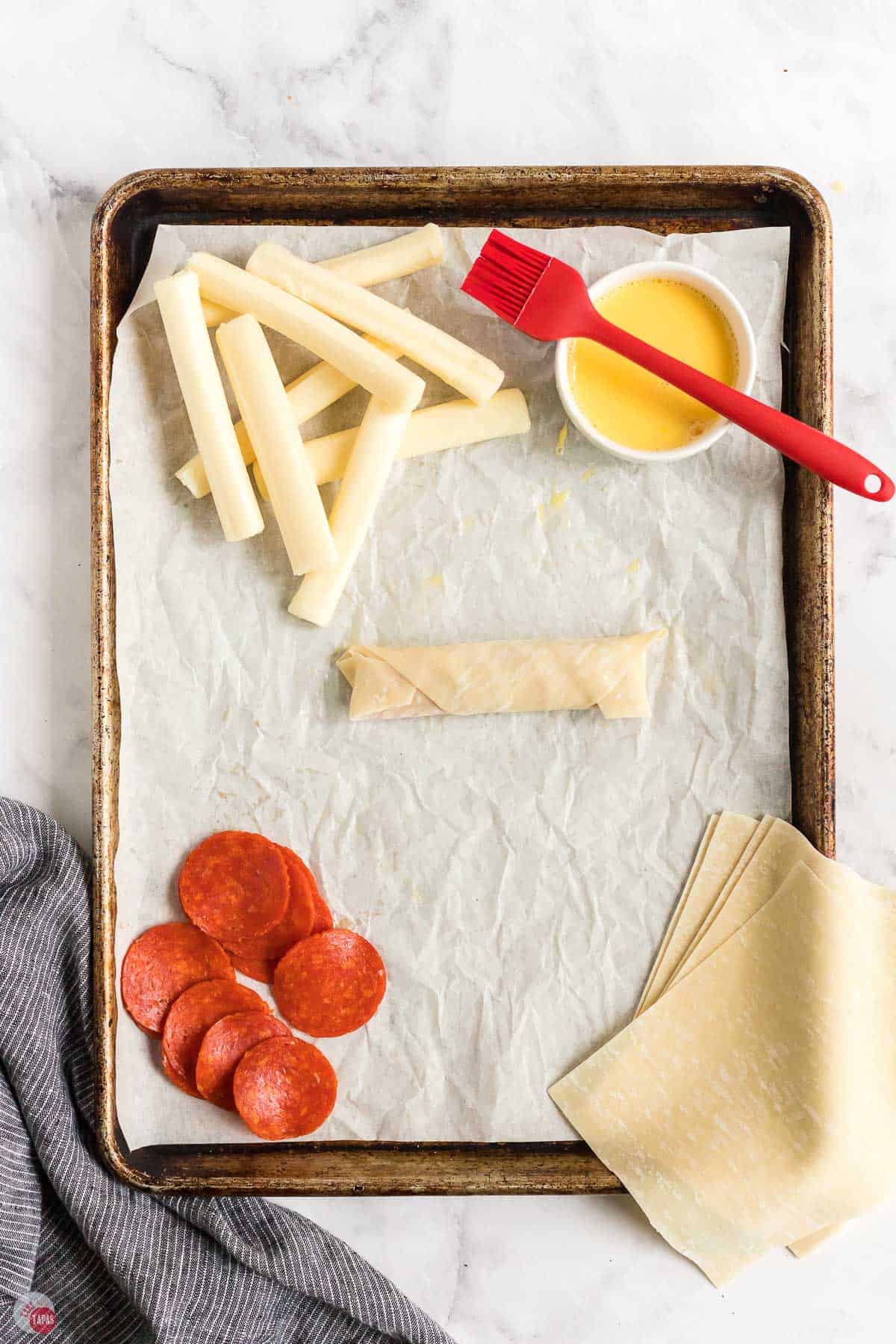 egg roll on a baking sheet surrounded by pepperoni