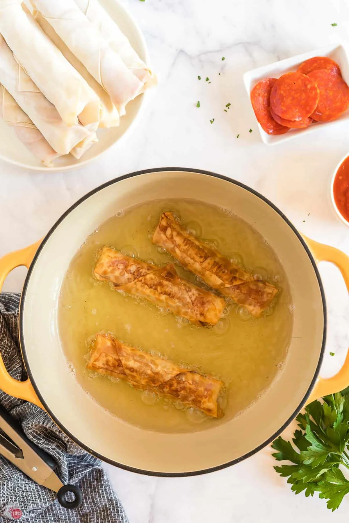 pizza egg rolls being fried in oil in a yellow pot
