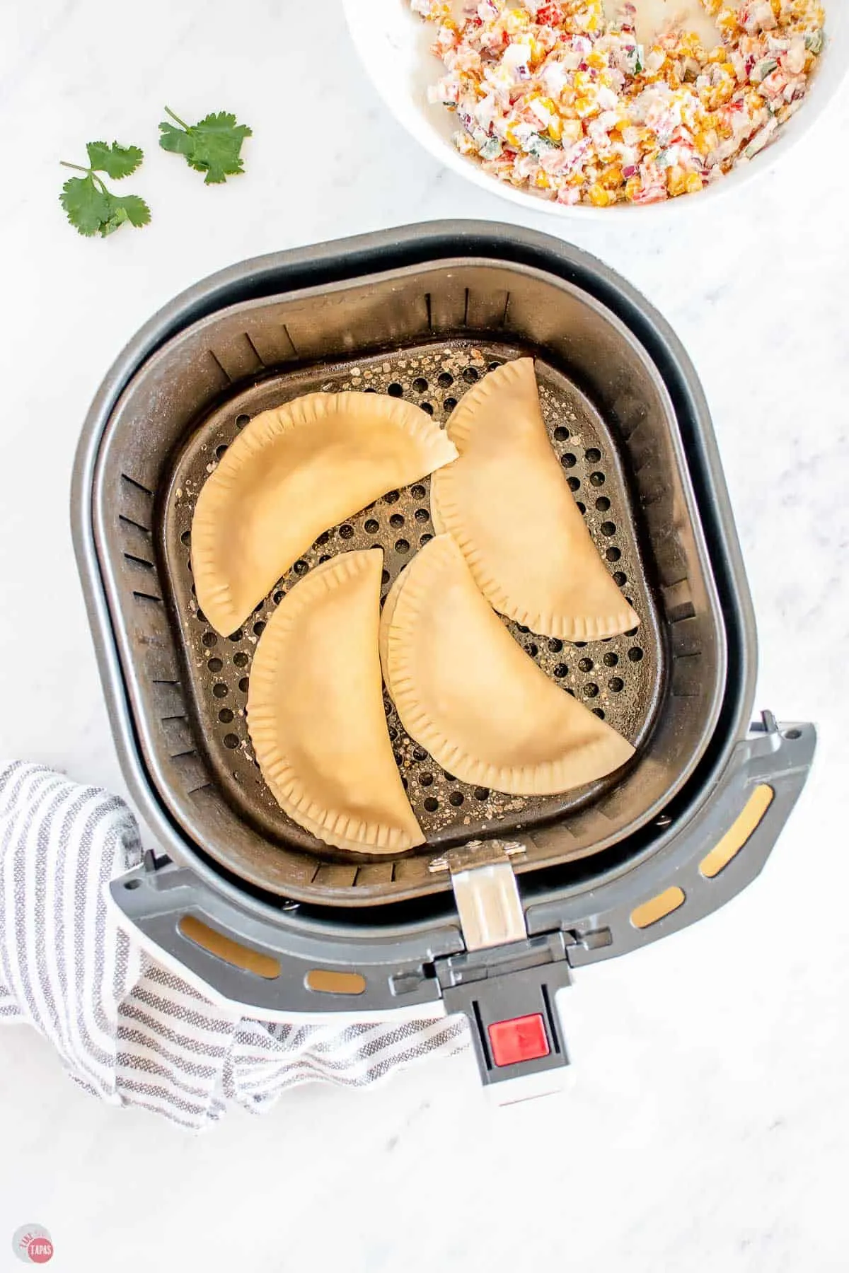 uncooked empanadas in an air fryer basket
