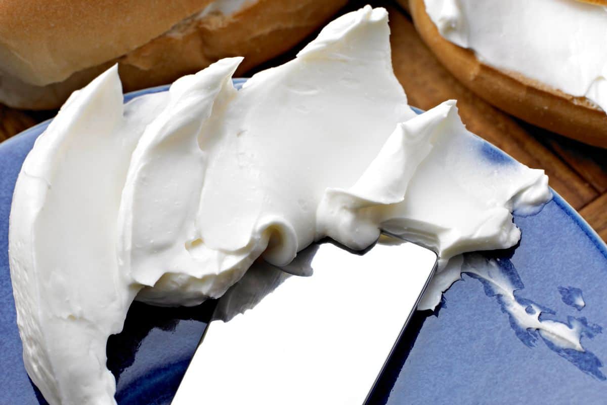 knife smearing cream cheese on a blue board