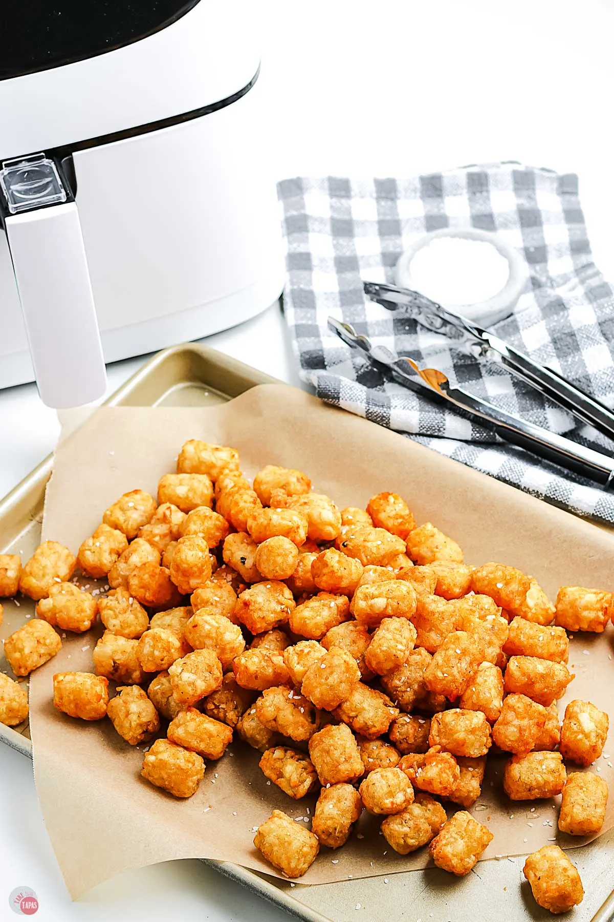 baking sheet with tater tots and a pair of tongs