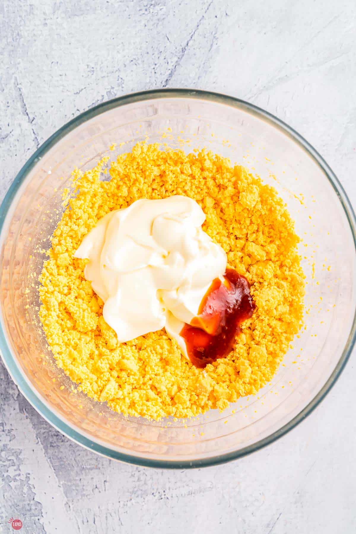 crumbled egg yolk with mayo and sriracha in a clear bowl