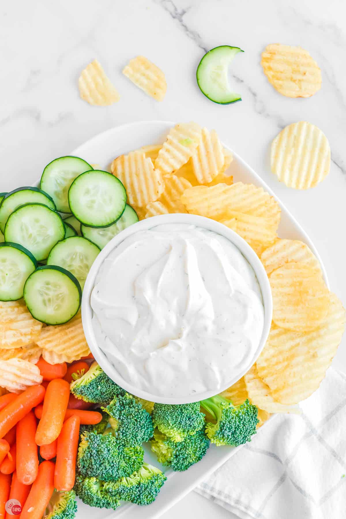 dip surrounded by chips and fresh chopped vegetables