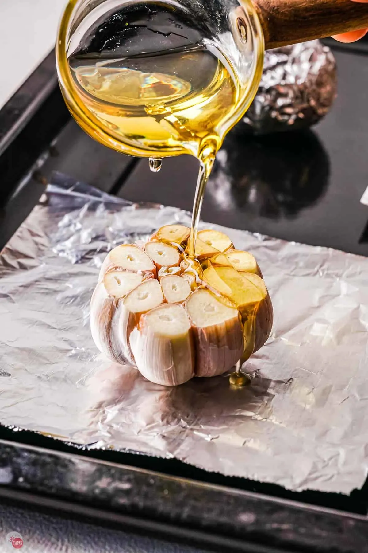 oil being drizzled on top of the garlic head on piece of foil