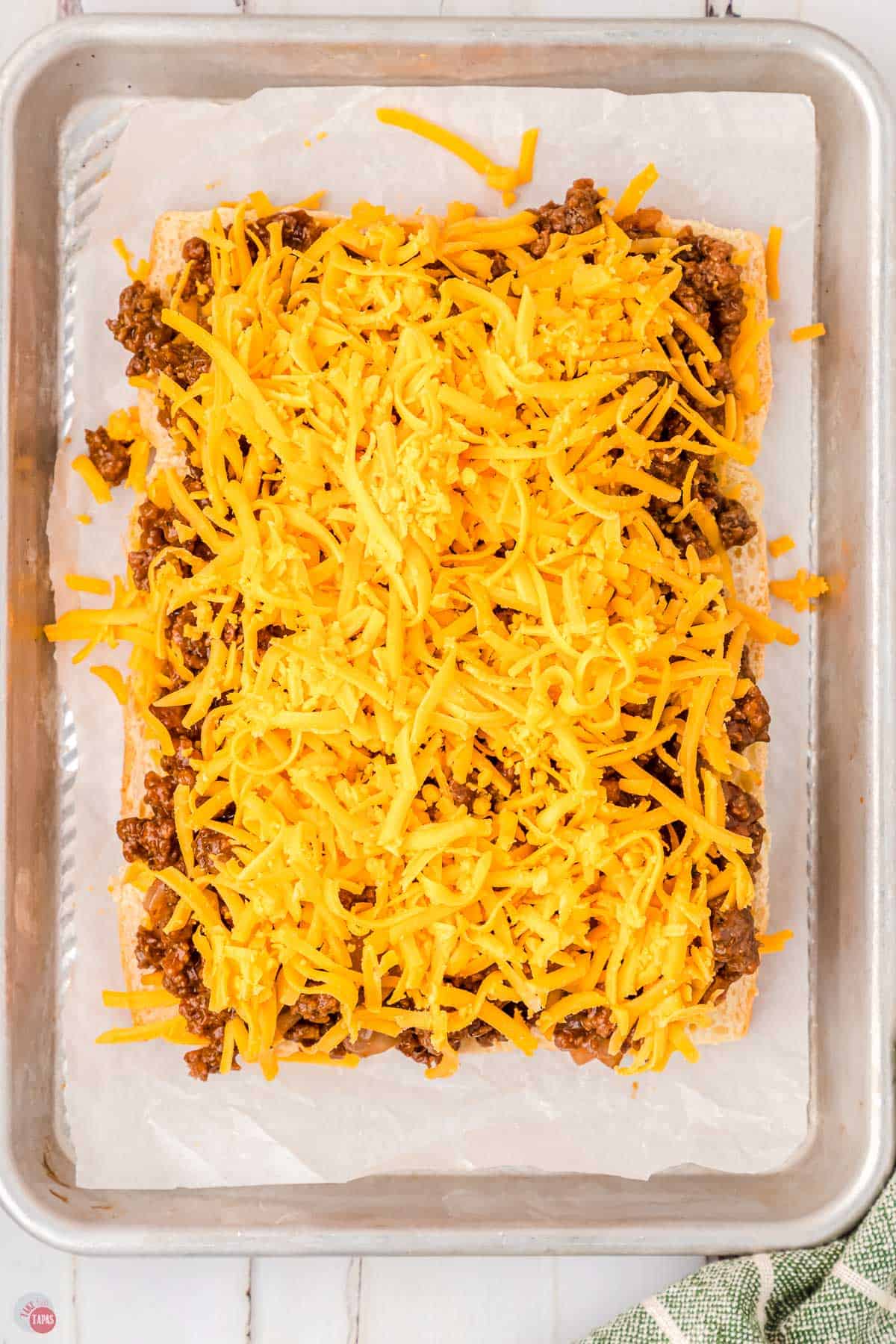 bottom slider buns topped with a ground beef mixture and shredded cheese