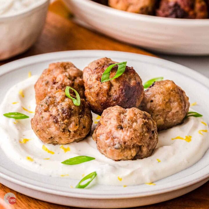 lamb meatballs on a plate with tzatziki sauce and green onions