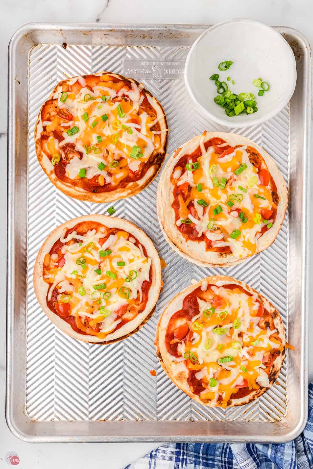 mexican pizzas topped with mexican blend cheese on a baking sheet