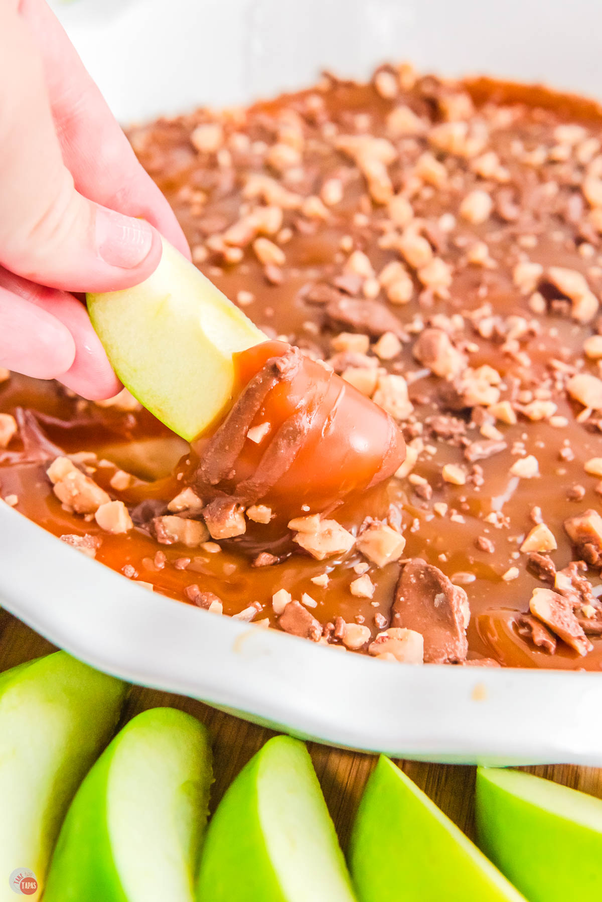 homemade caramel apple dip with a hand and apple slice.