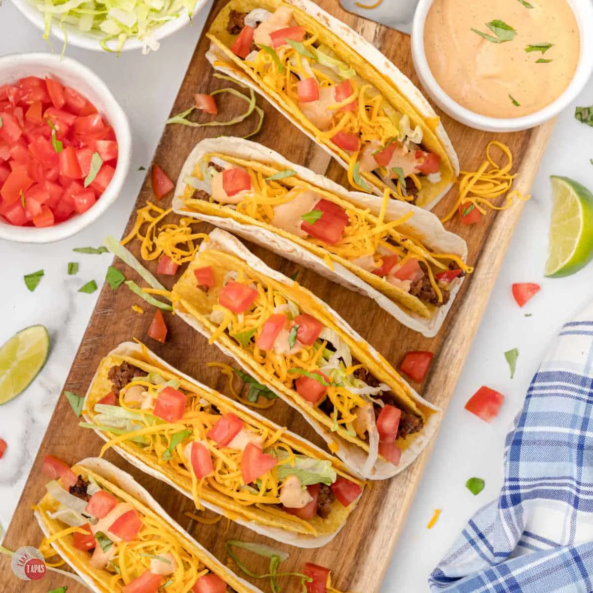 tray of tacos next to bowls of lime wedges and diced tomatoes