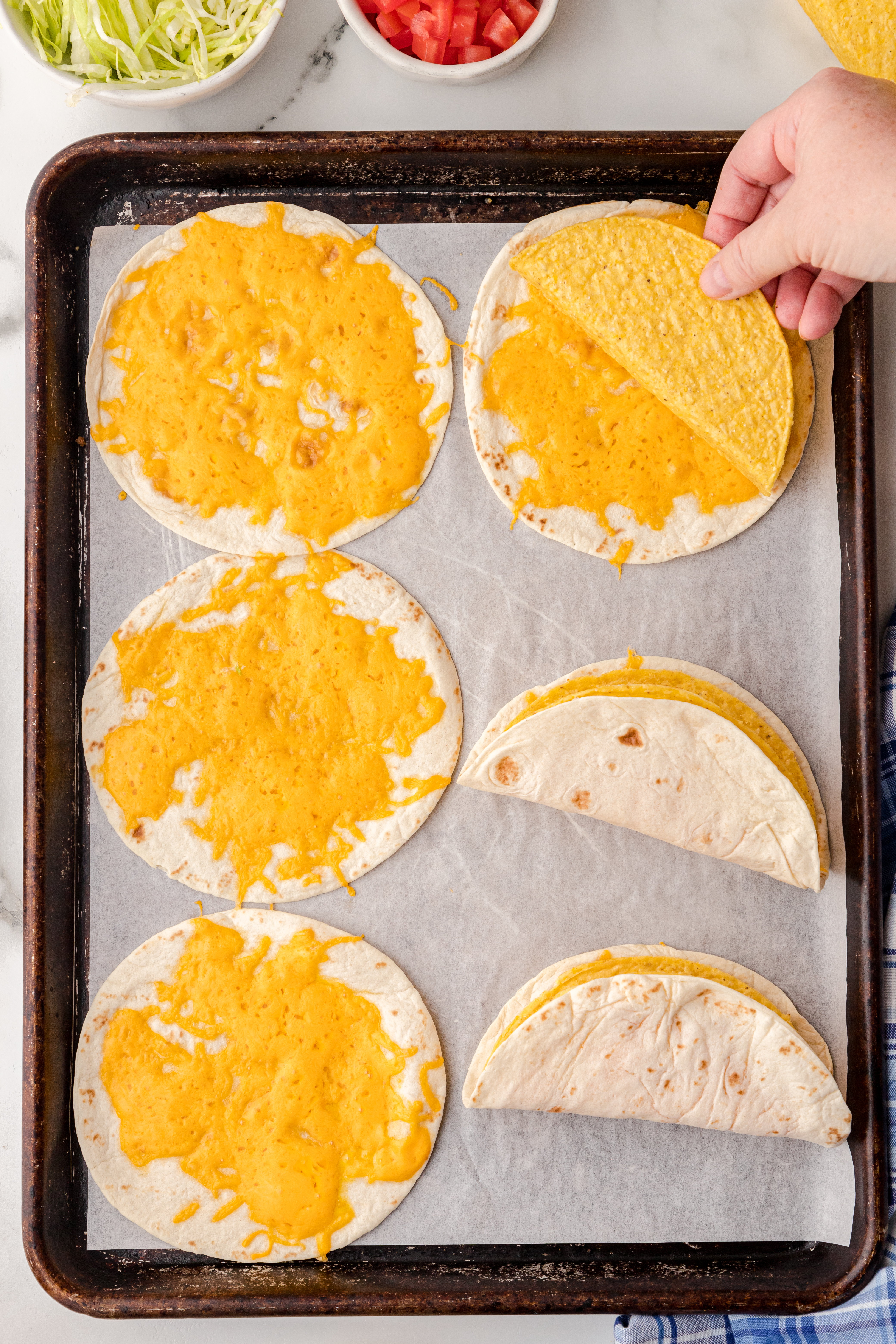 soft and hard shell tacos on a baking sheet with cheese between them