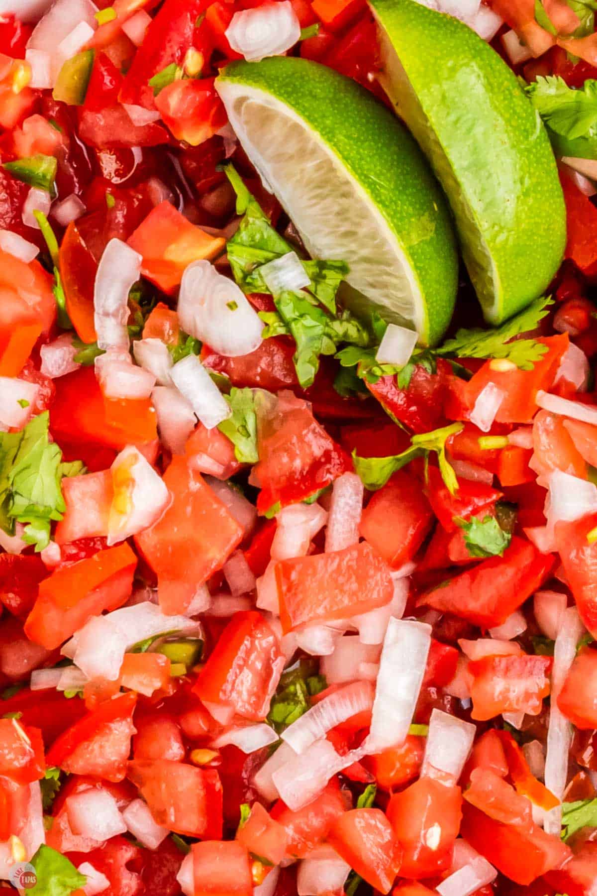 close up of pico de gallo in a bowl with lime wedges