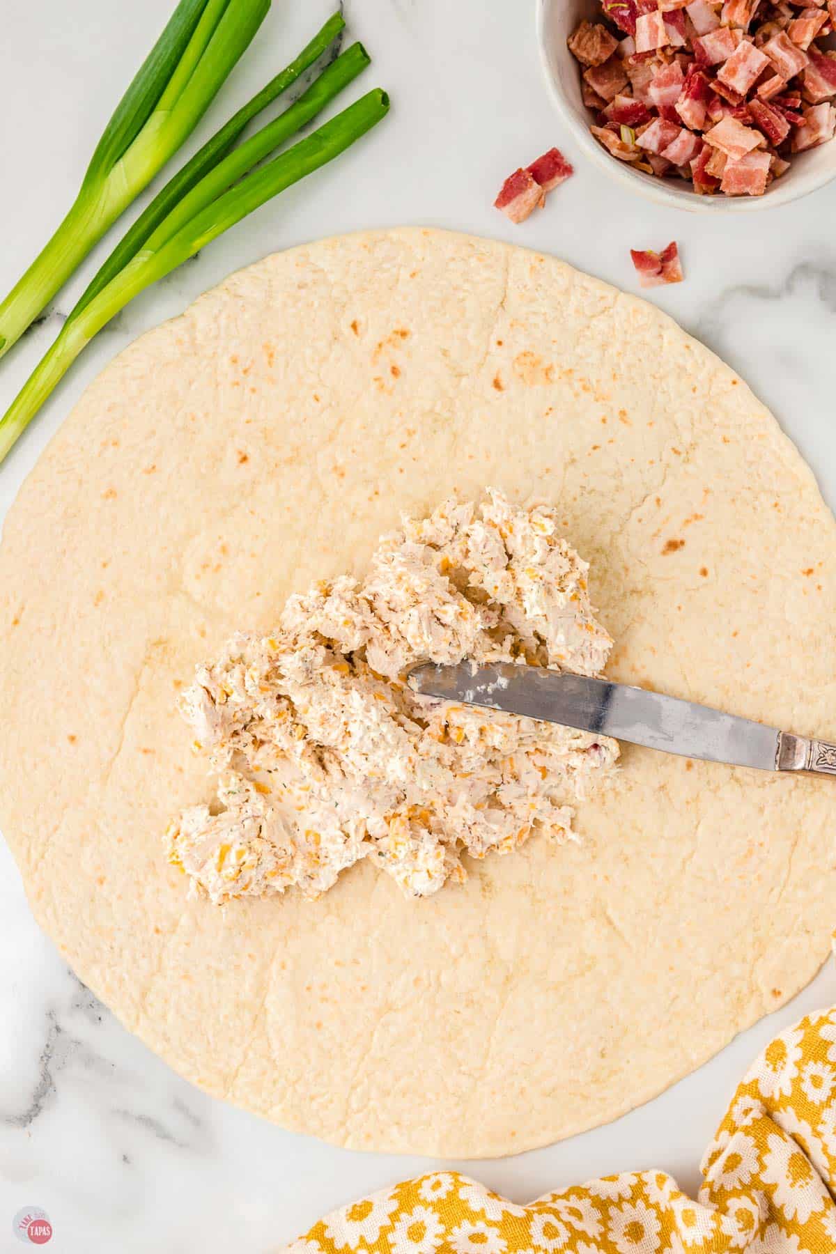 offset spatula spreading cream cheese and chicken on a flour tortilla