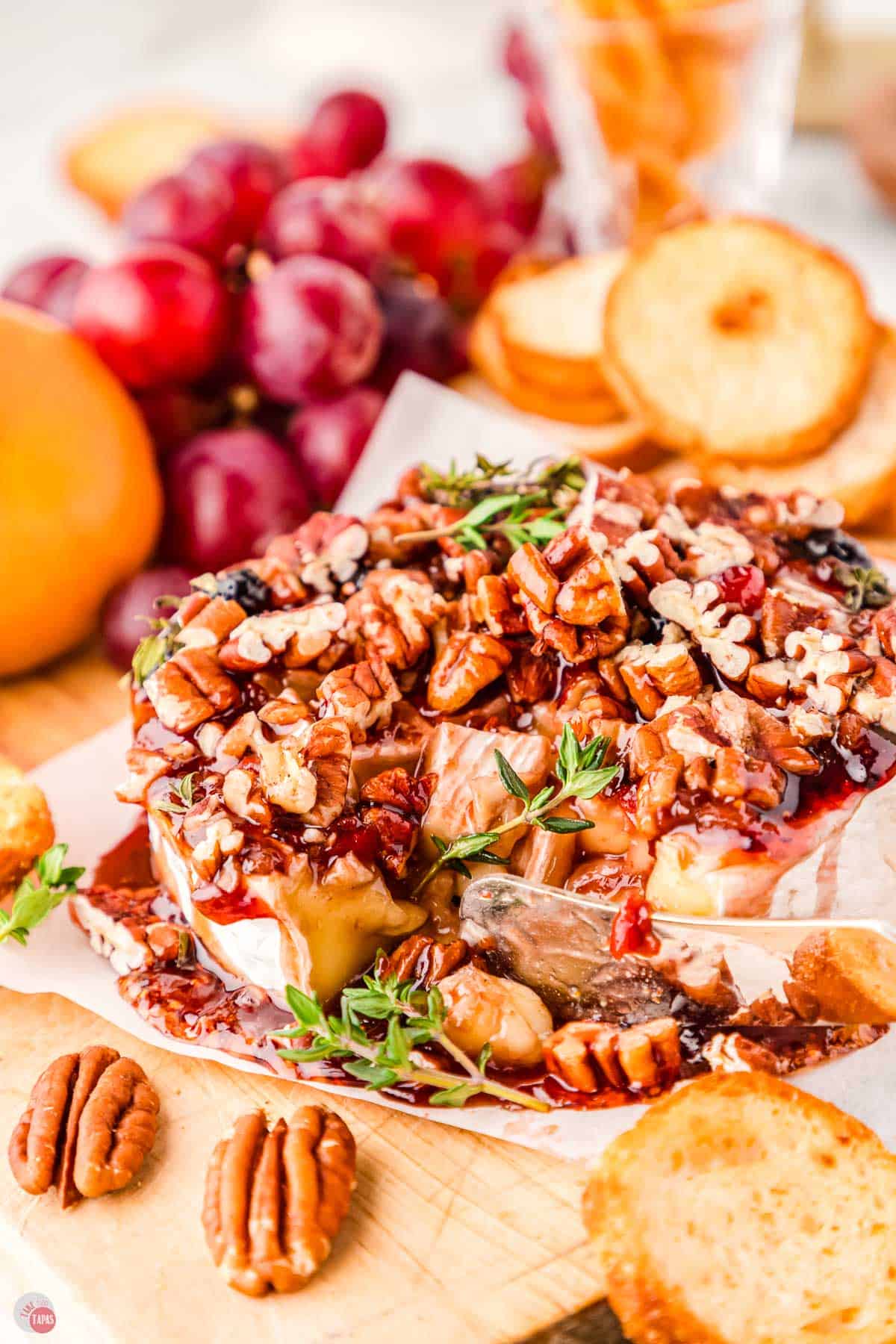 knife cutting into a wheel of brie topped with jam and nuts