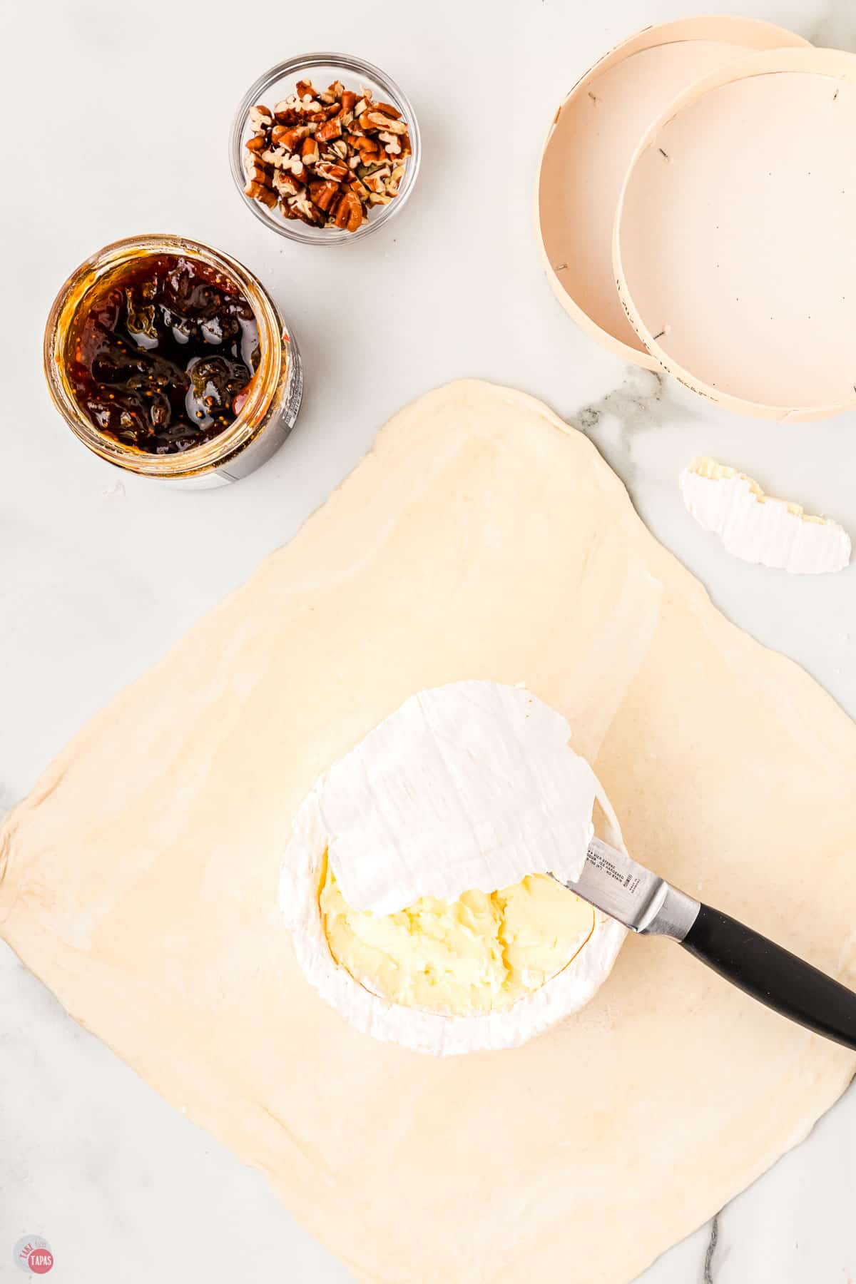 cheese knife cutting the rind off of a brie wheel