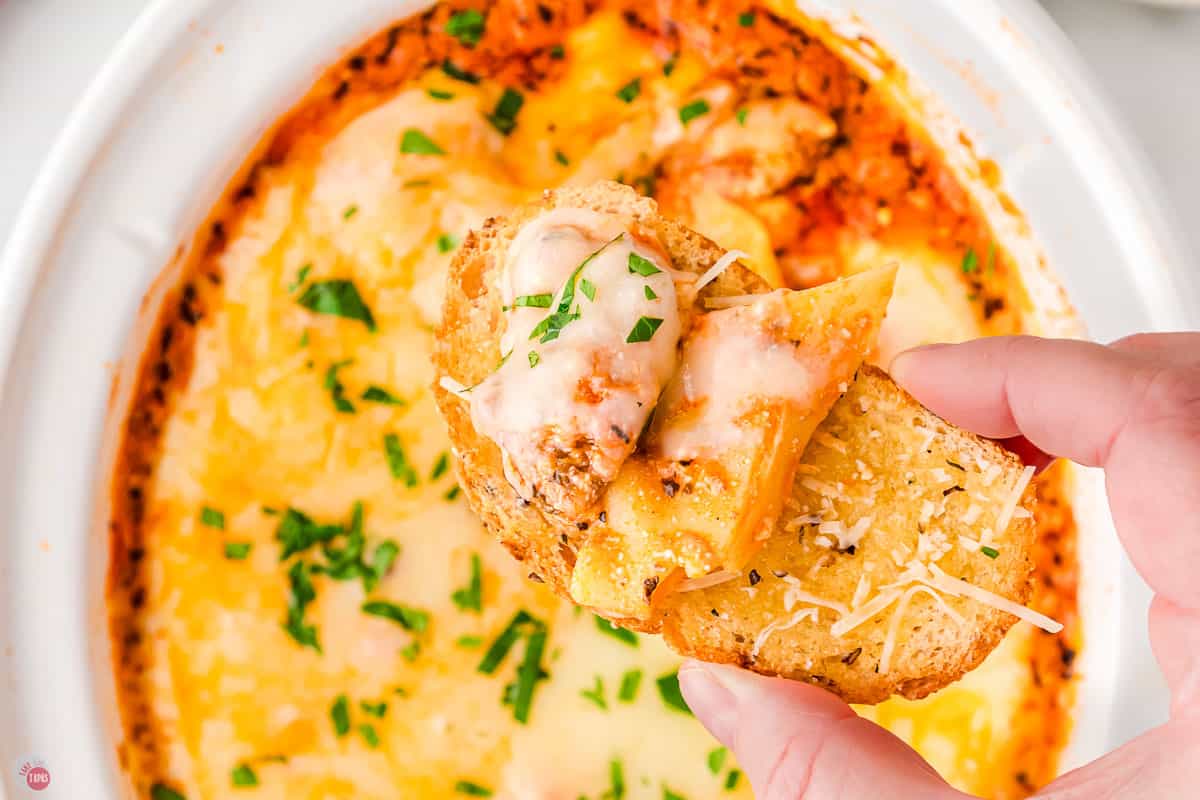 hand holding crostini with lasagna dip on it