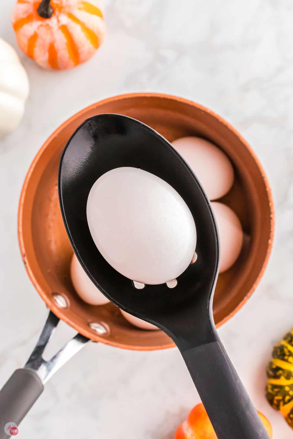spoon holding a hard boiled egg over a copper pot
