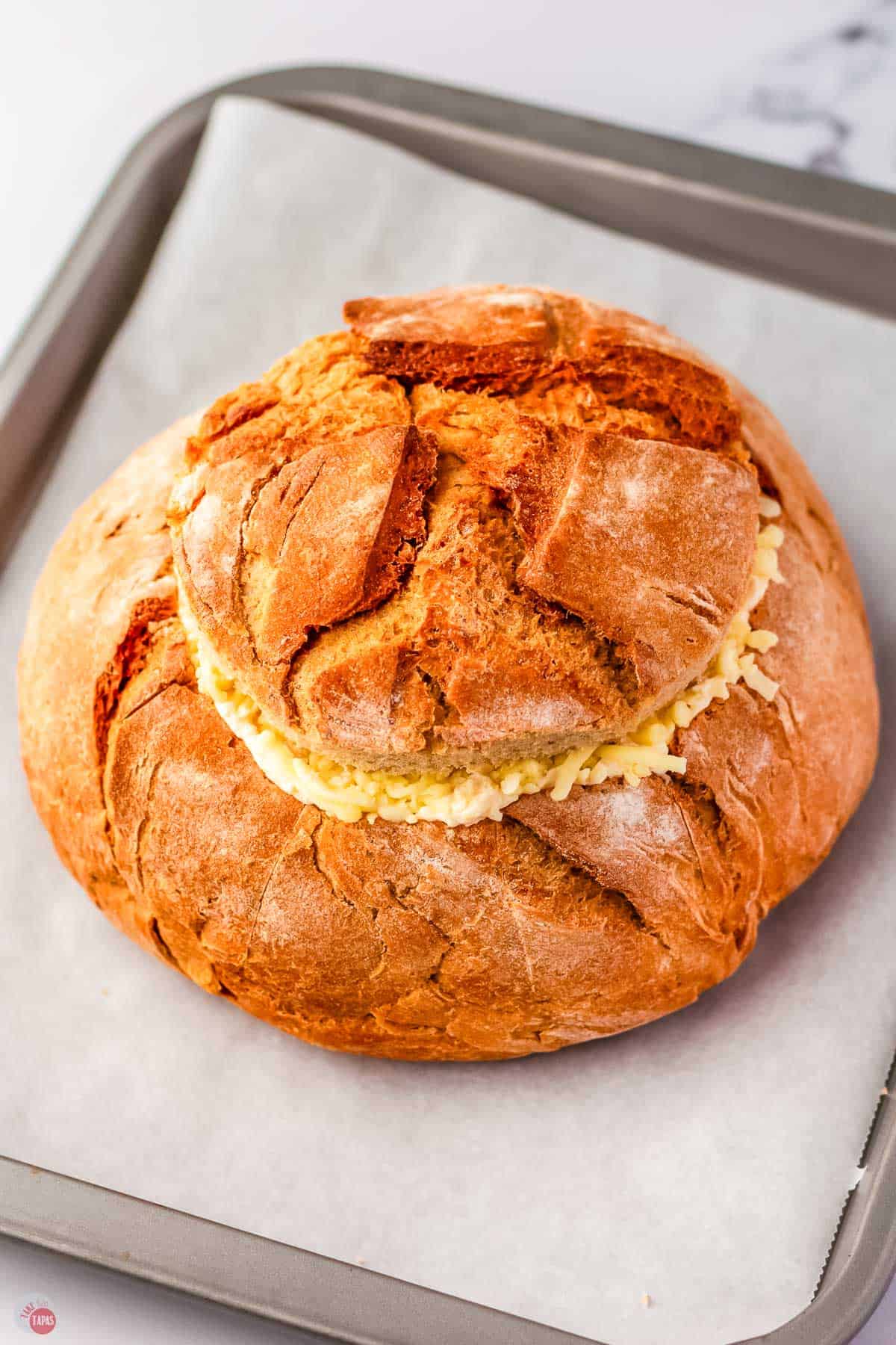 bread bowl, stuffed with cheese, with the top put back on, on a baking sheet