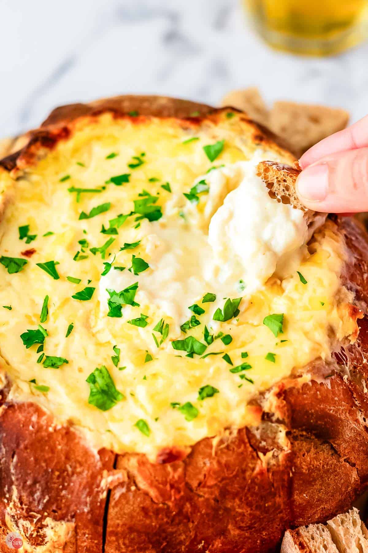 hand holding a piece of bread and dipping it into melted cheese
