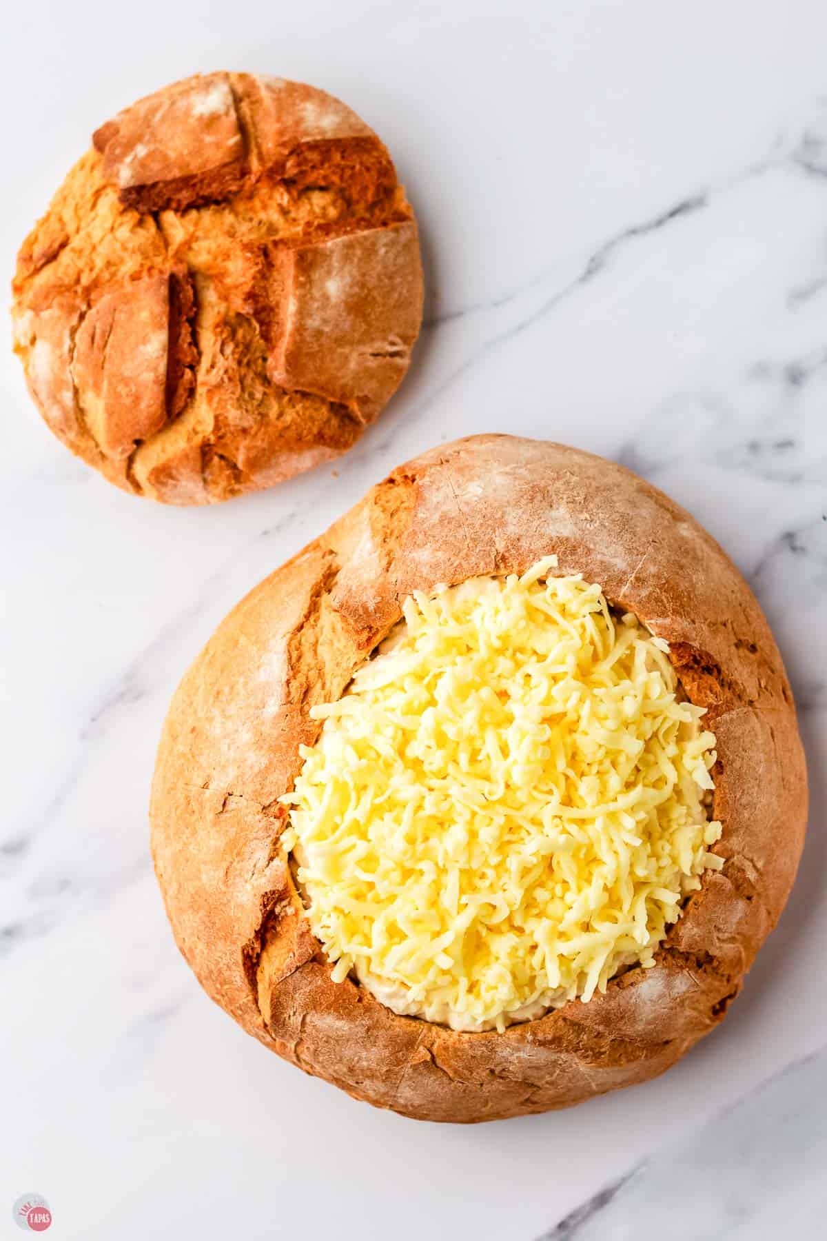 bread loaf with dip in it and shredded cheese on top