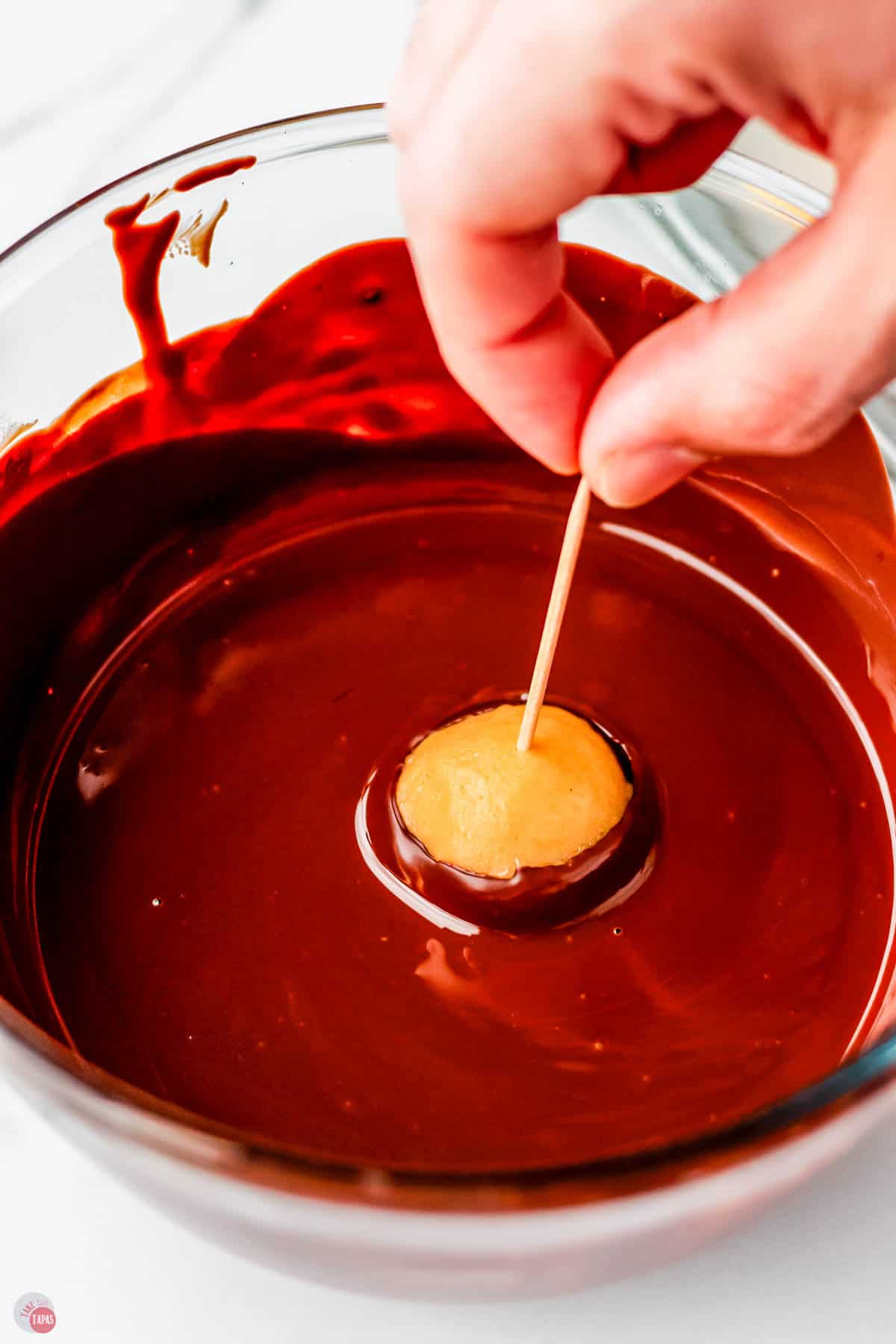 peanut butter buckeye on a toothpick being dipped in melted chocolate