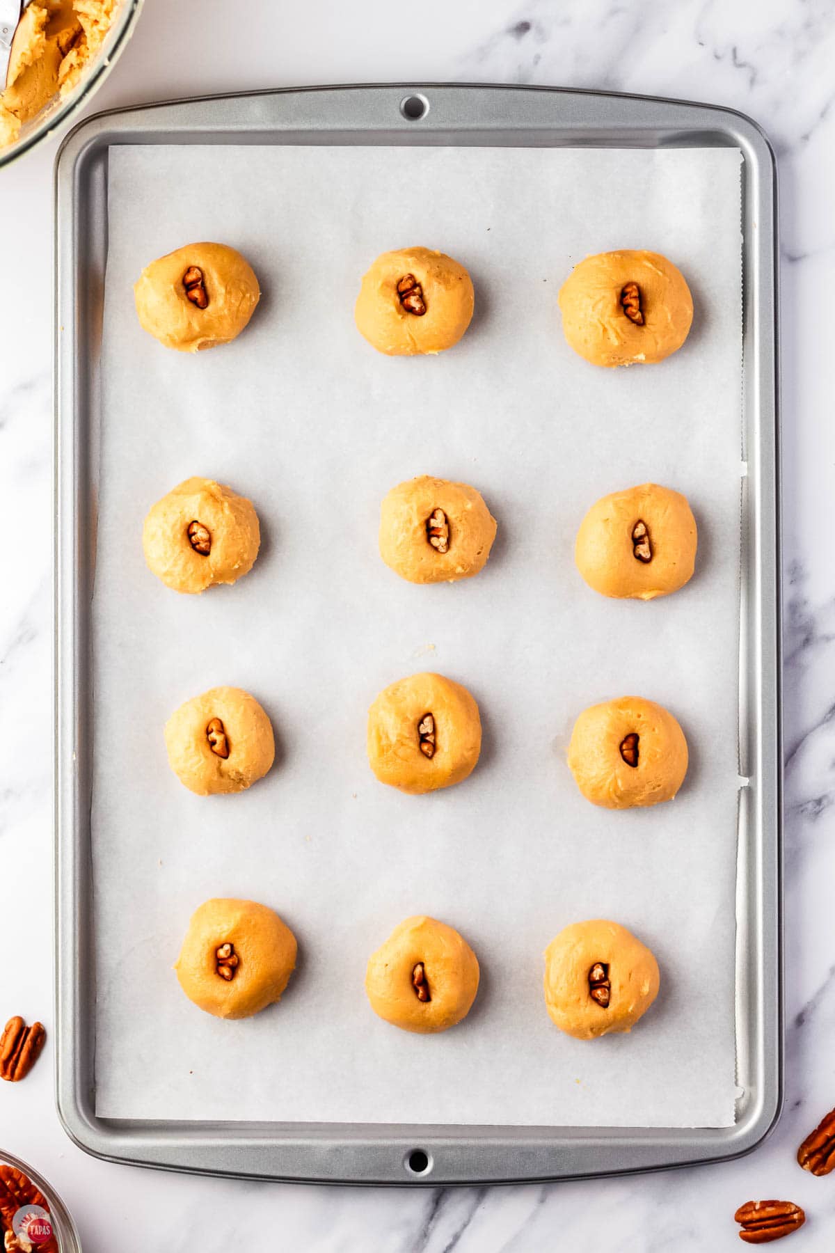peanut butter balls on a baking sheet with parchment paper with a pecan half stuffed into each one