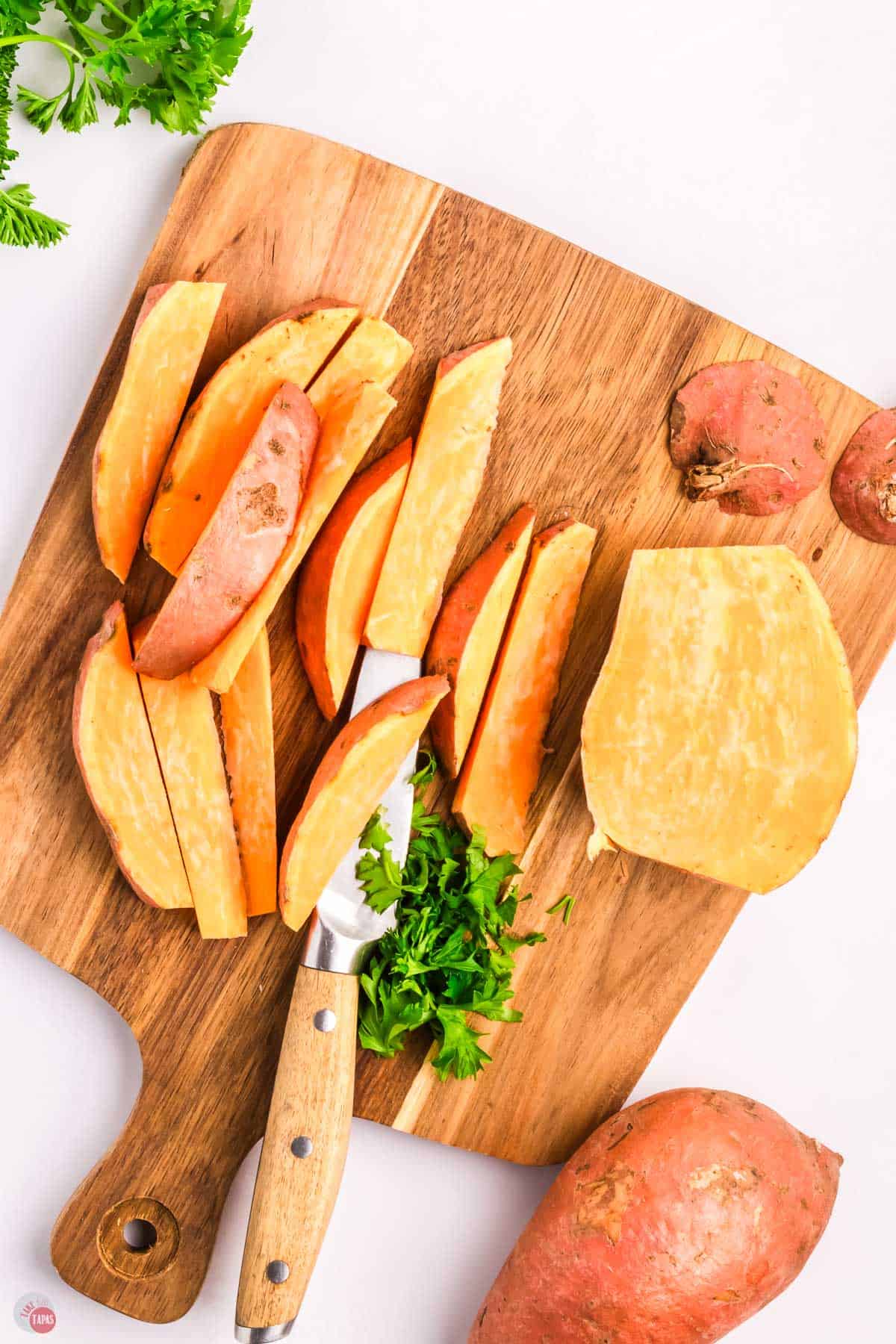 sweet potatoes on a cutting board with a knife being cut into wedges