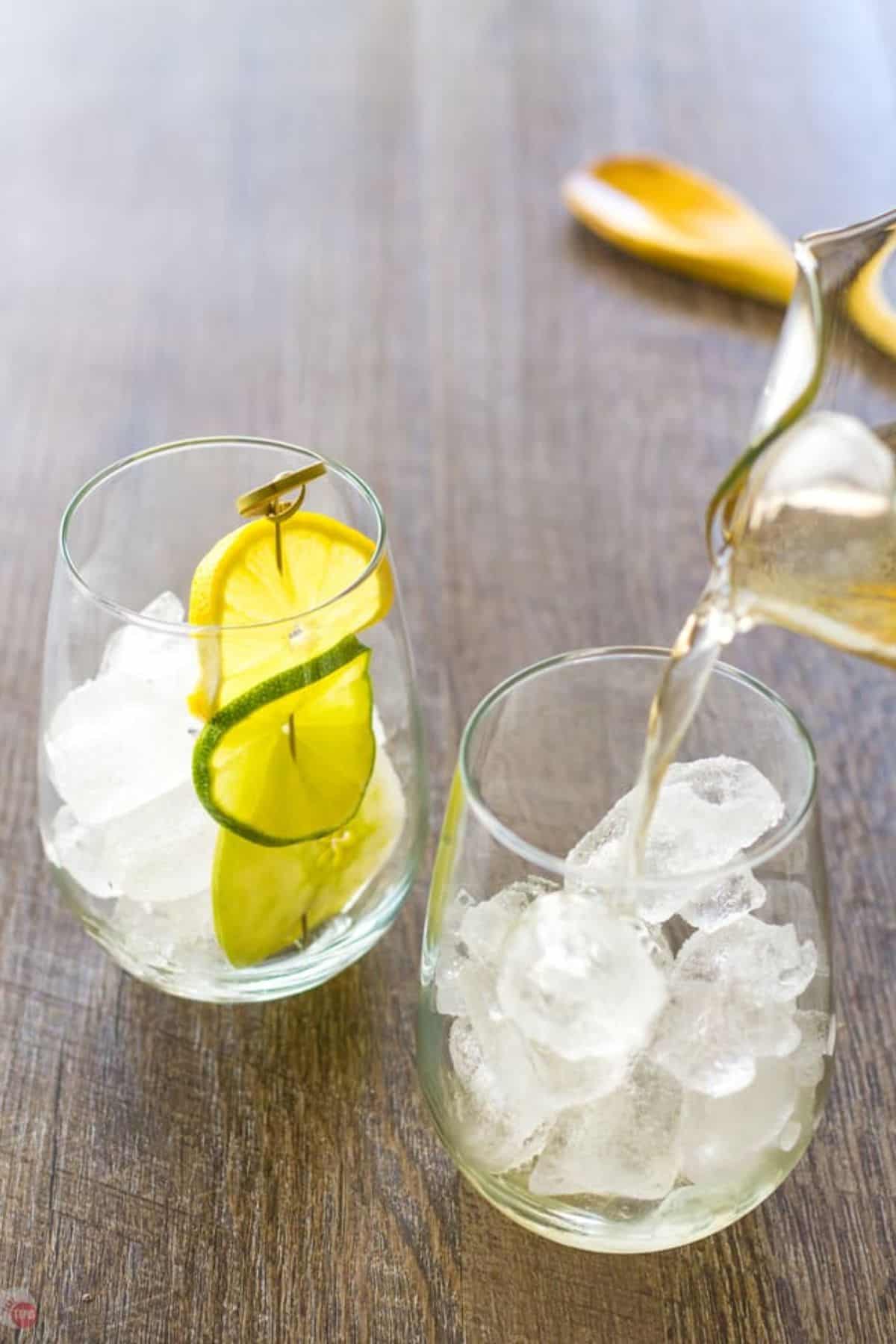 pitcher pouring sangria into a wine glass with ice cubes and lime slices in it