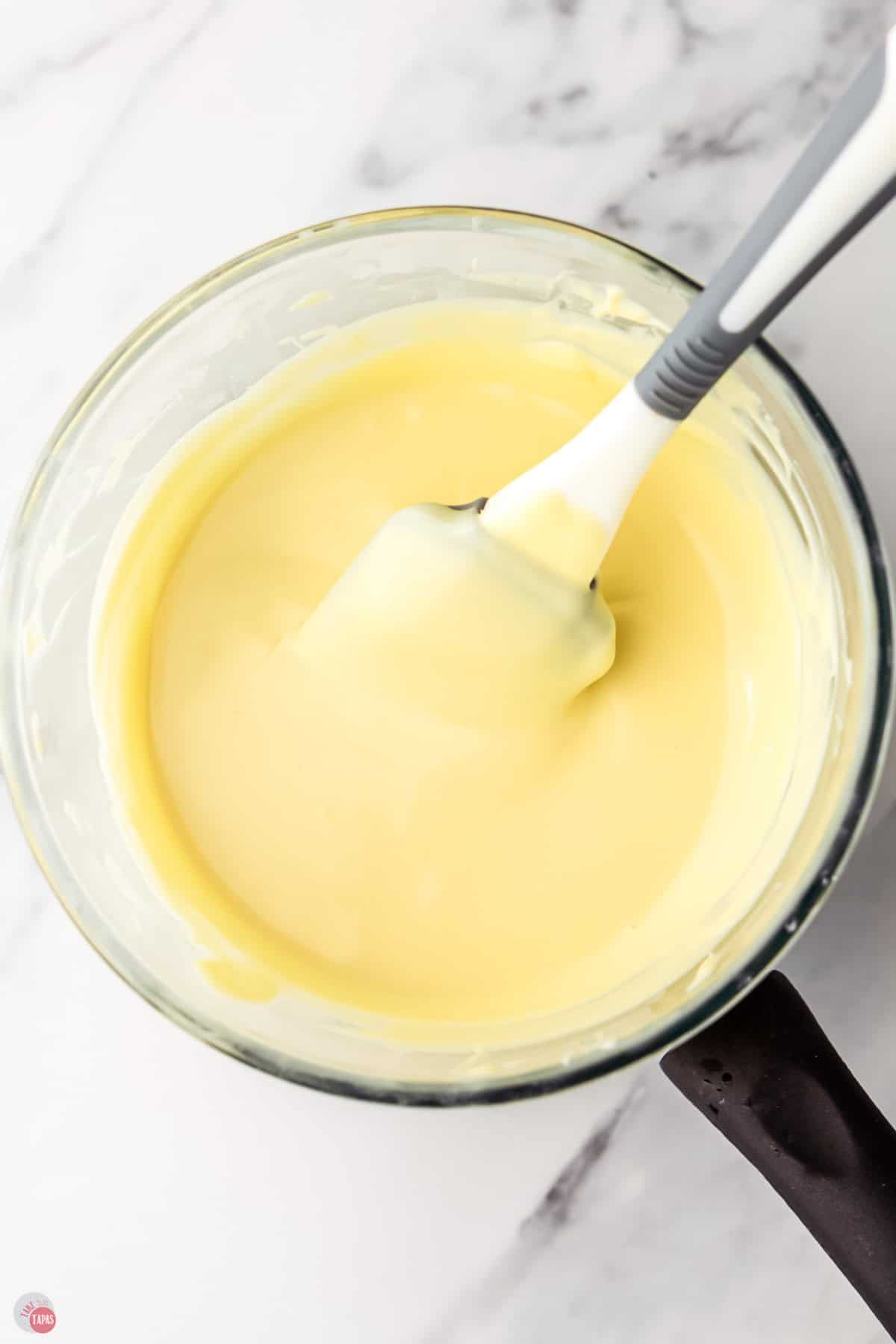 melted white chocolate in a clear bowl with a spatula