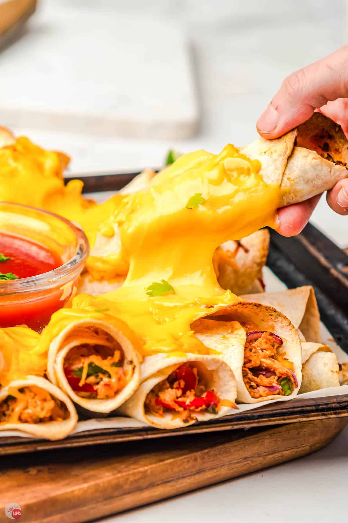 hand pulling a wrapped tortilla off a stack of them on a baking sheet