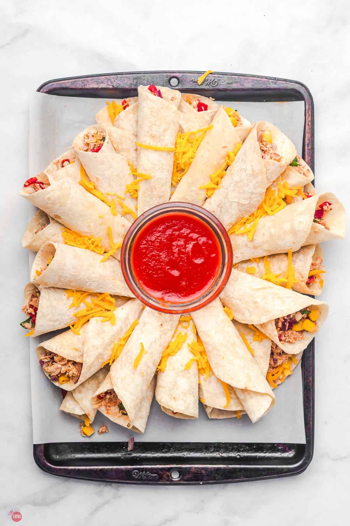 baking sheet with rolled tortillas on it and a bowl of salsa in the middle