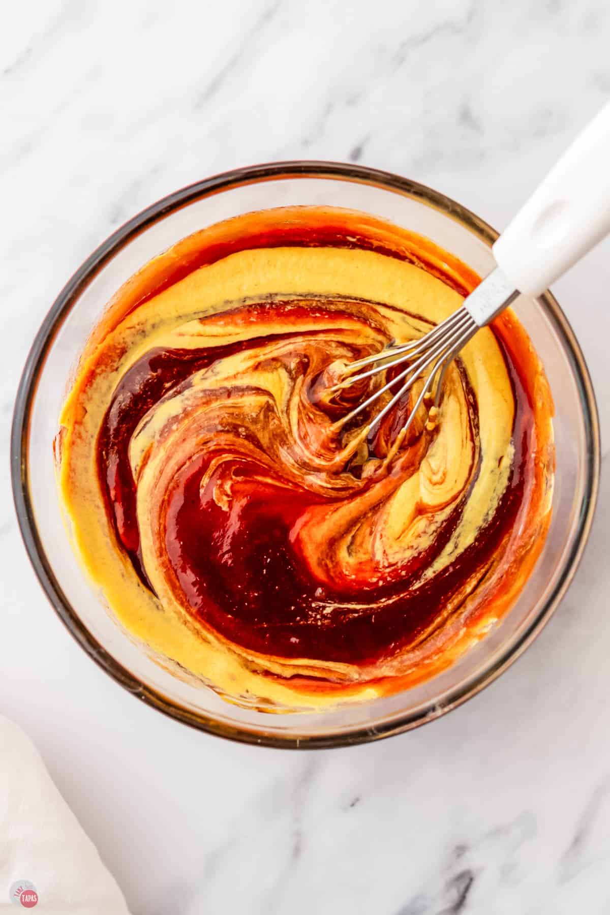 bbq sauce and mustard being mixed together in a clear bowl with a whisk