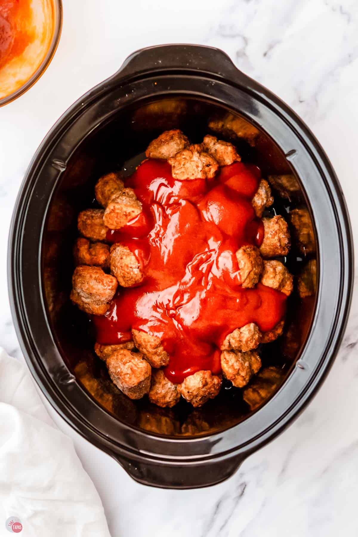 frozen meatballs in a crock pot with sauce poured over them
