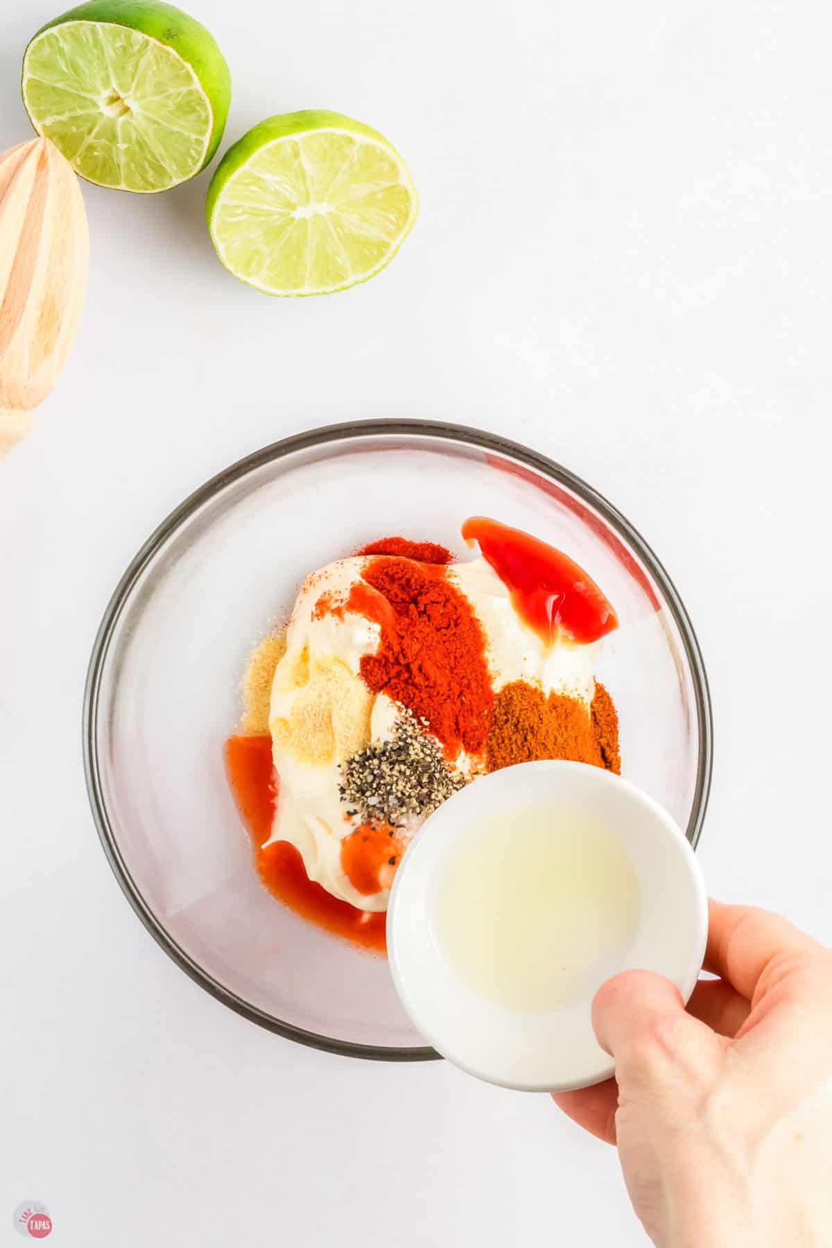 sauce ingredients in a clear bowl with a hand holding a small white bowl of lime juice above it