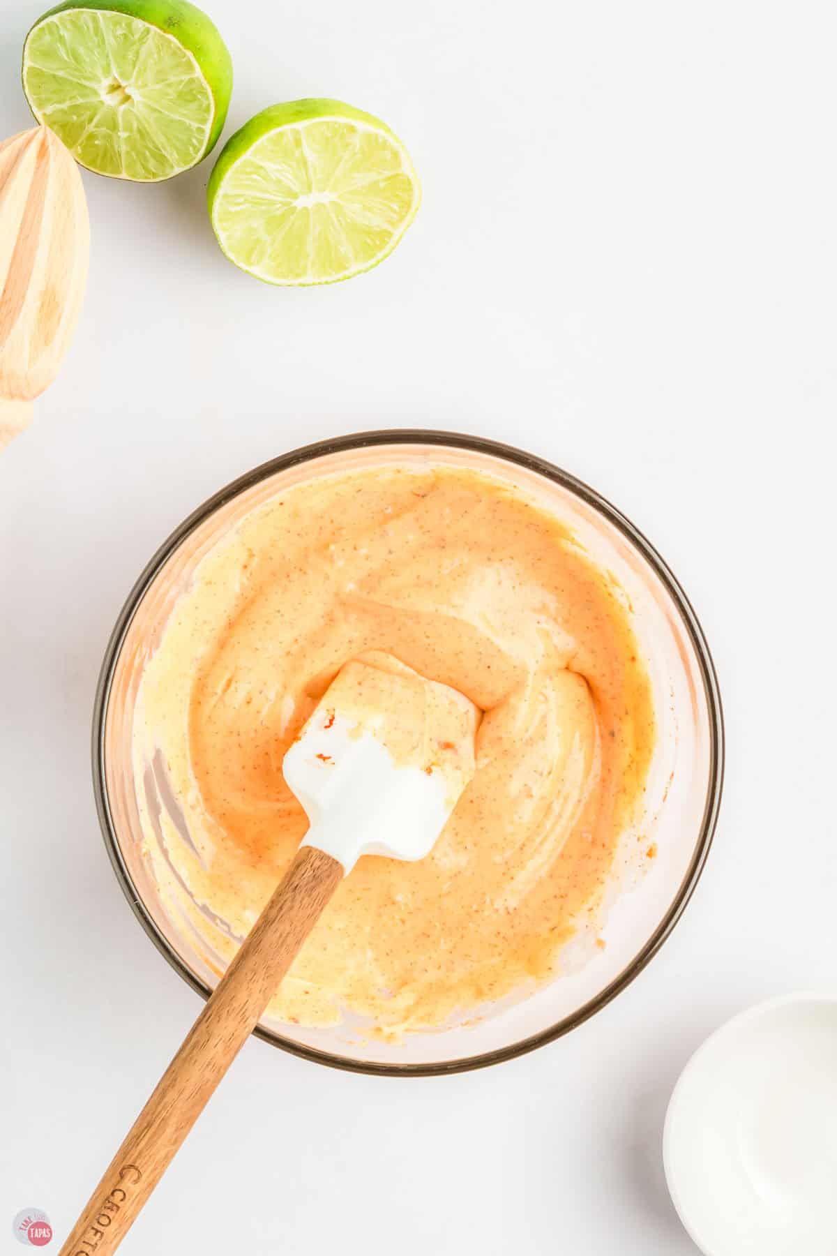clear bowl with orange sauce in it and a white spatula stirring it