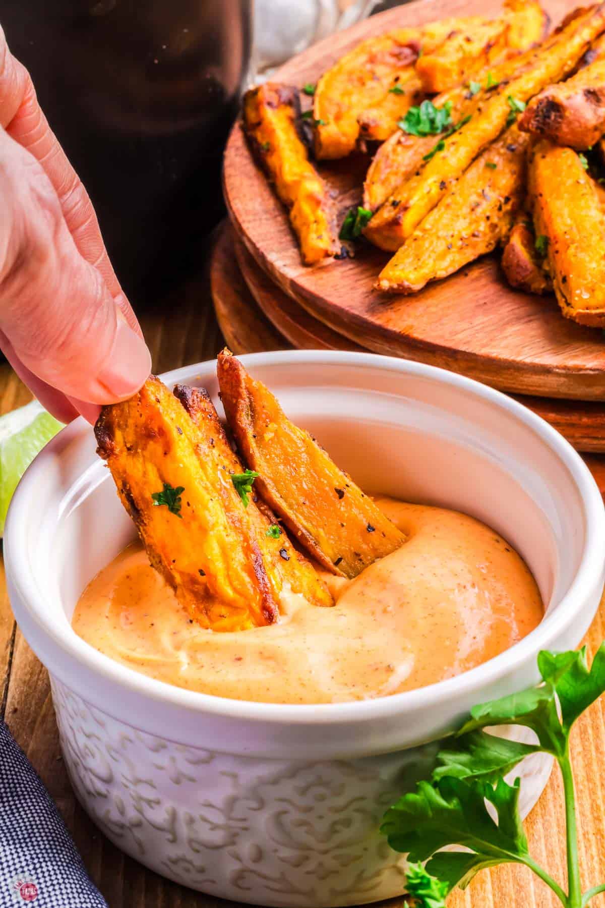 hand holding a french fry while dipping it in a small bowl of sauce