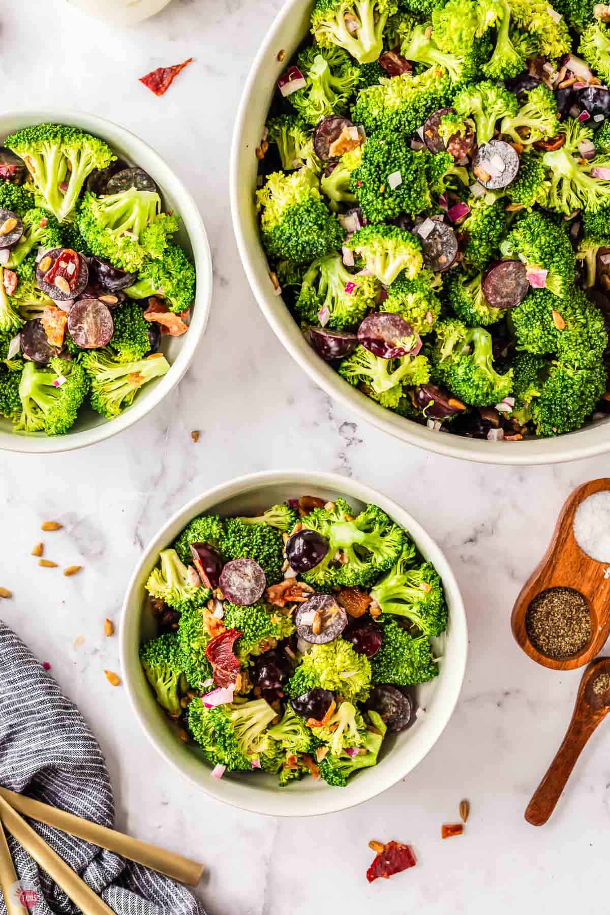 three bowls of broccoli grape salad on a marble table