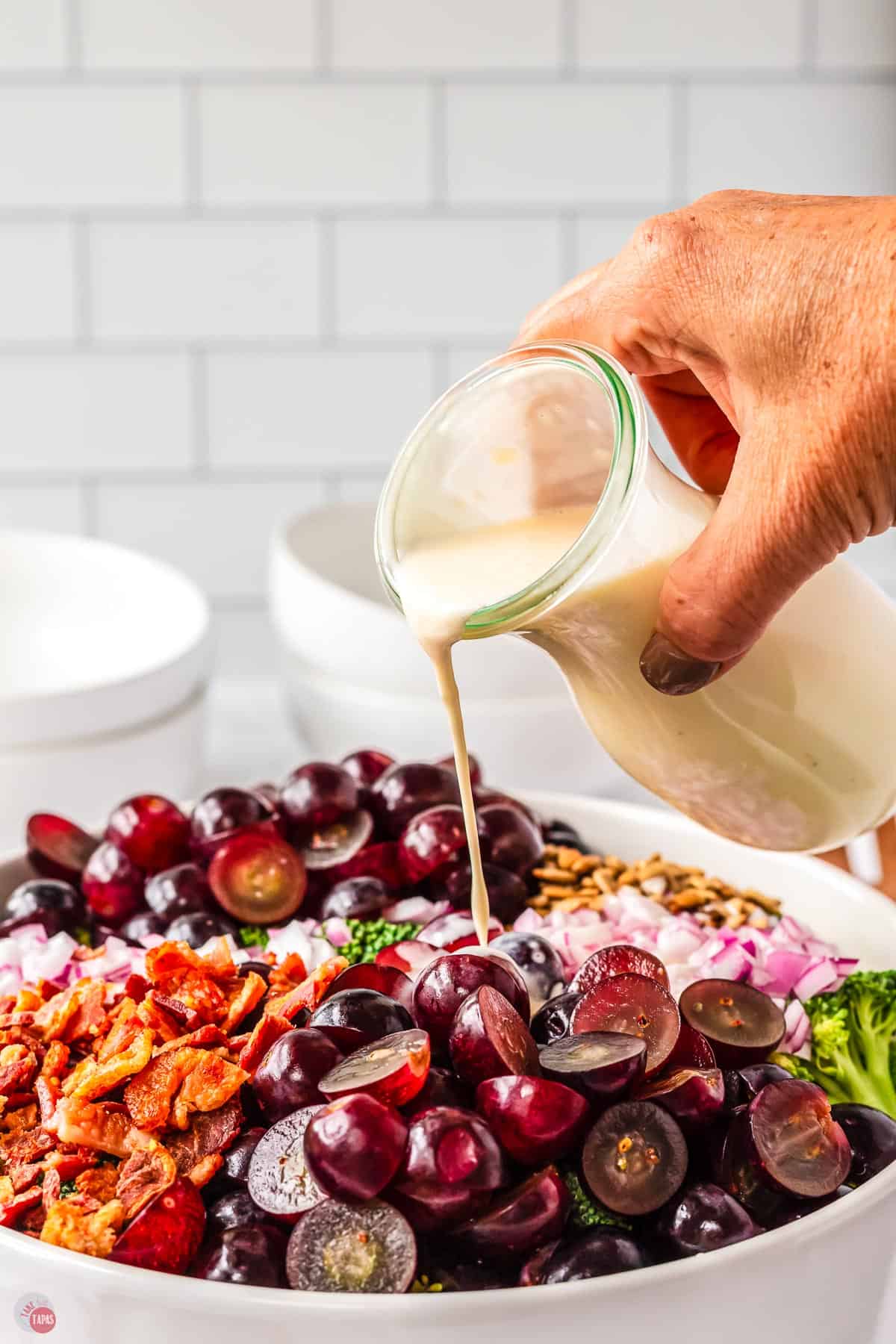 hand holding a bottle pouring dressing onto a salad