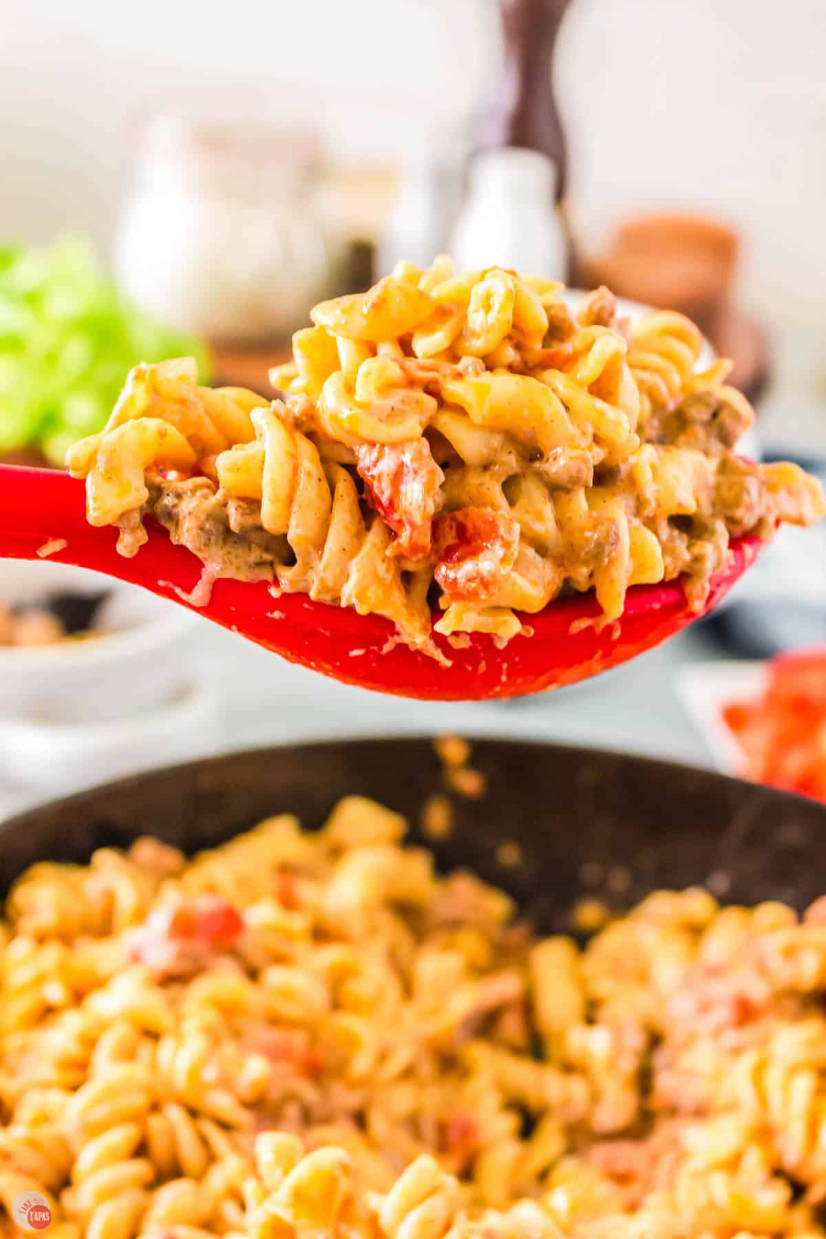 red spoon with a scoop of pasta in it above an iron skillet