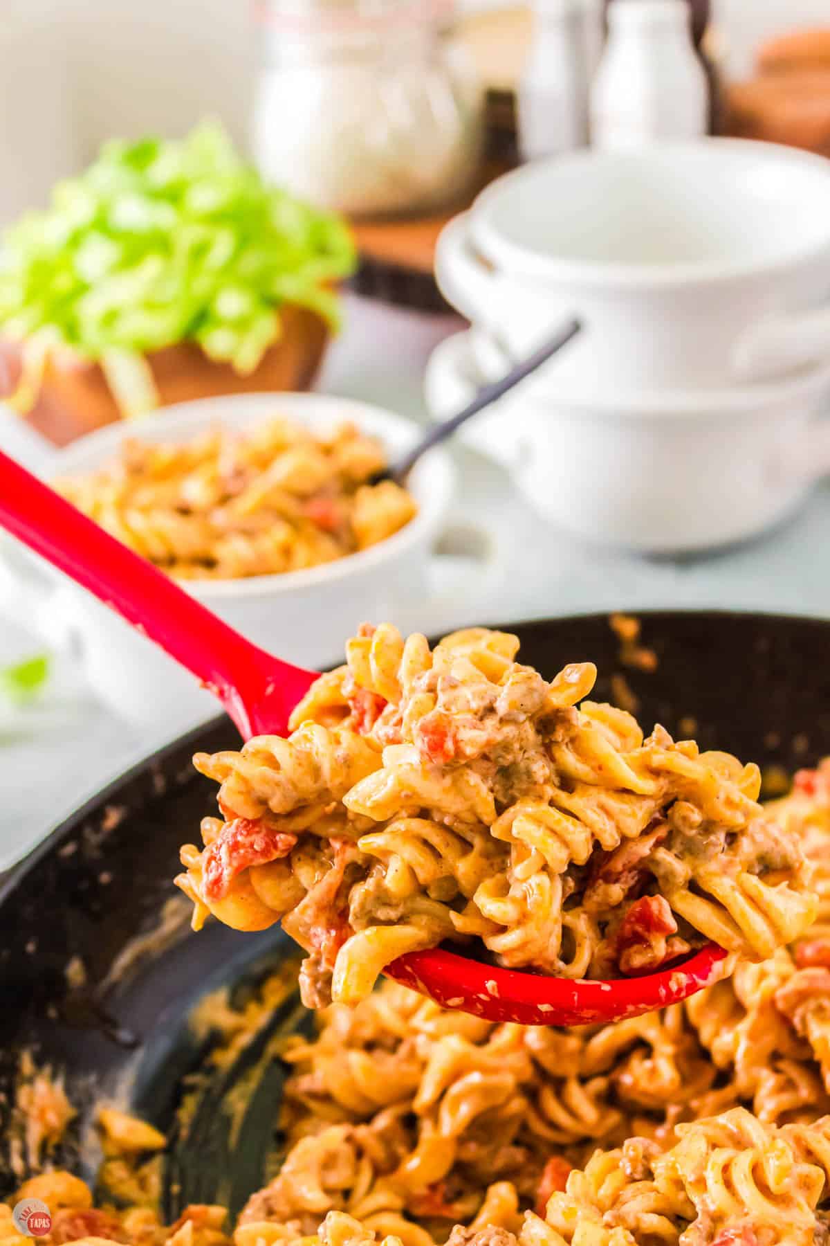 skillet of cheesy taco pasta with a red spoon