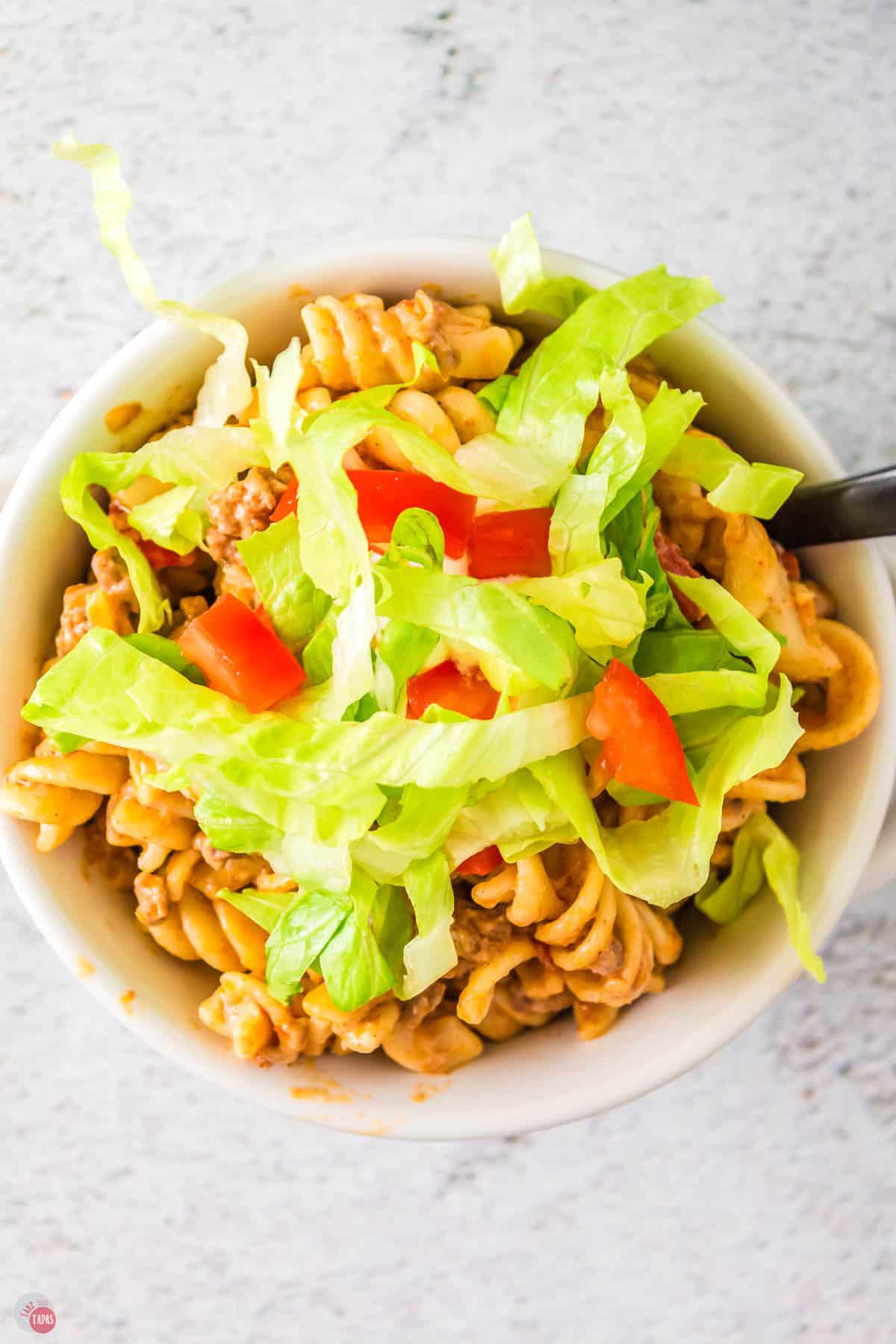 bowl of taco pasta topped with shredded lettuce and diced tomatoes