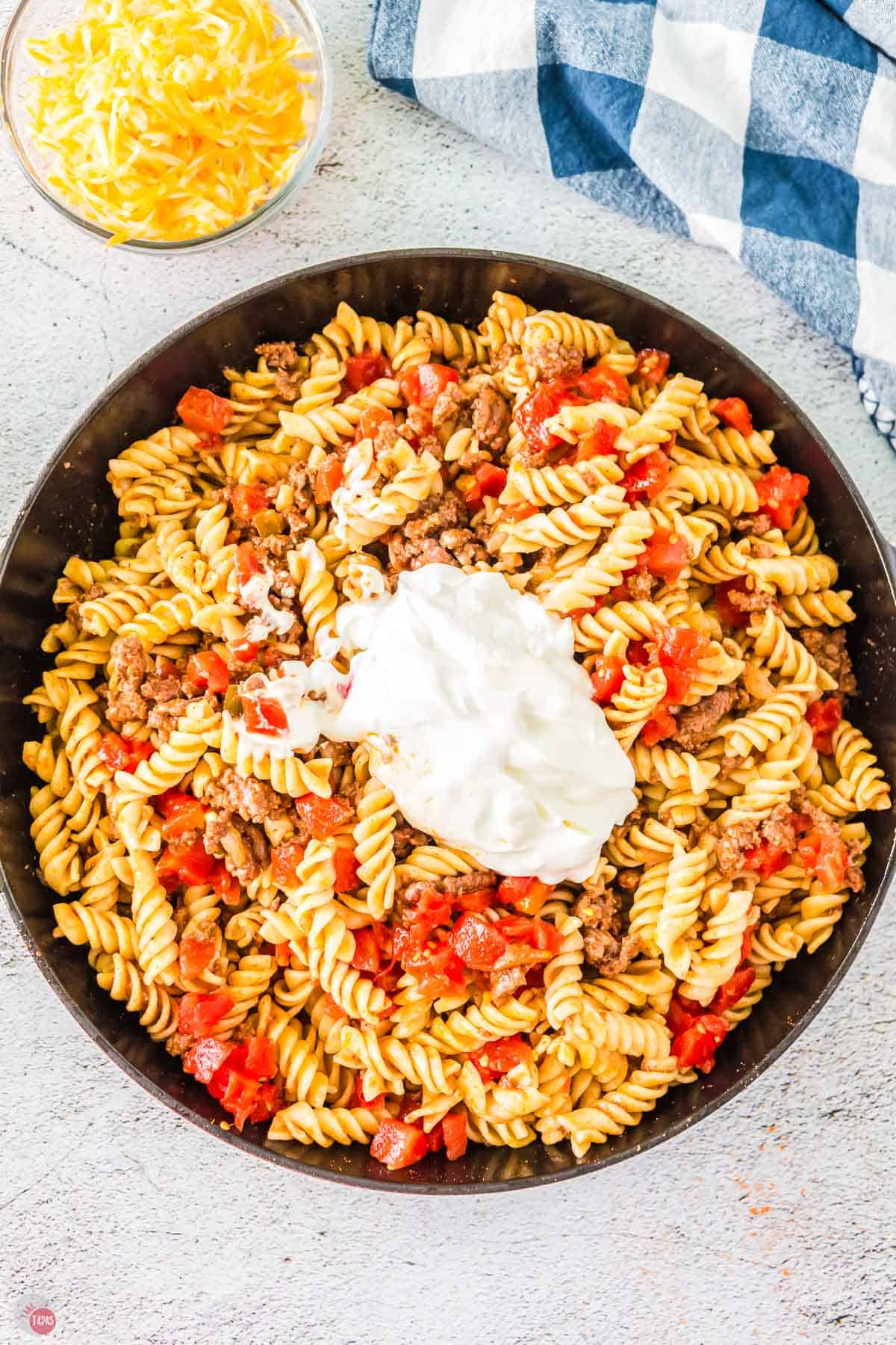 skillet with rotini pasta, cooked ground beef, diced tomatoes, topped with sour cream