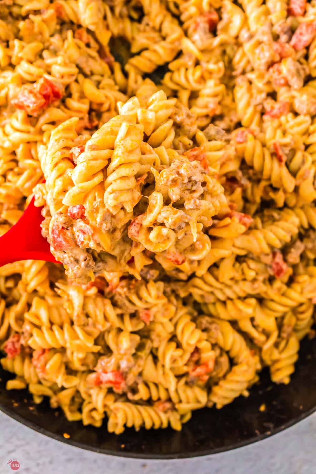 close up of beef taco pasta in it with a red spoon scooping some out
