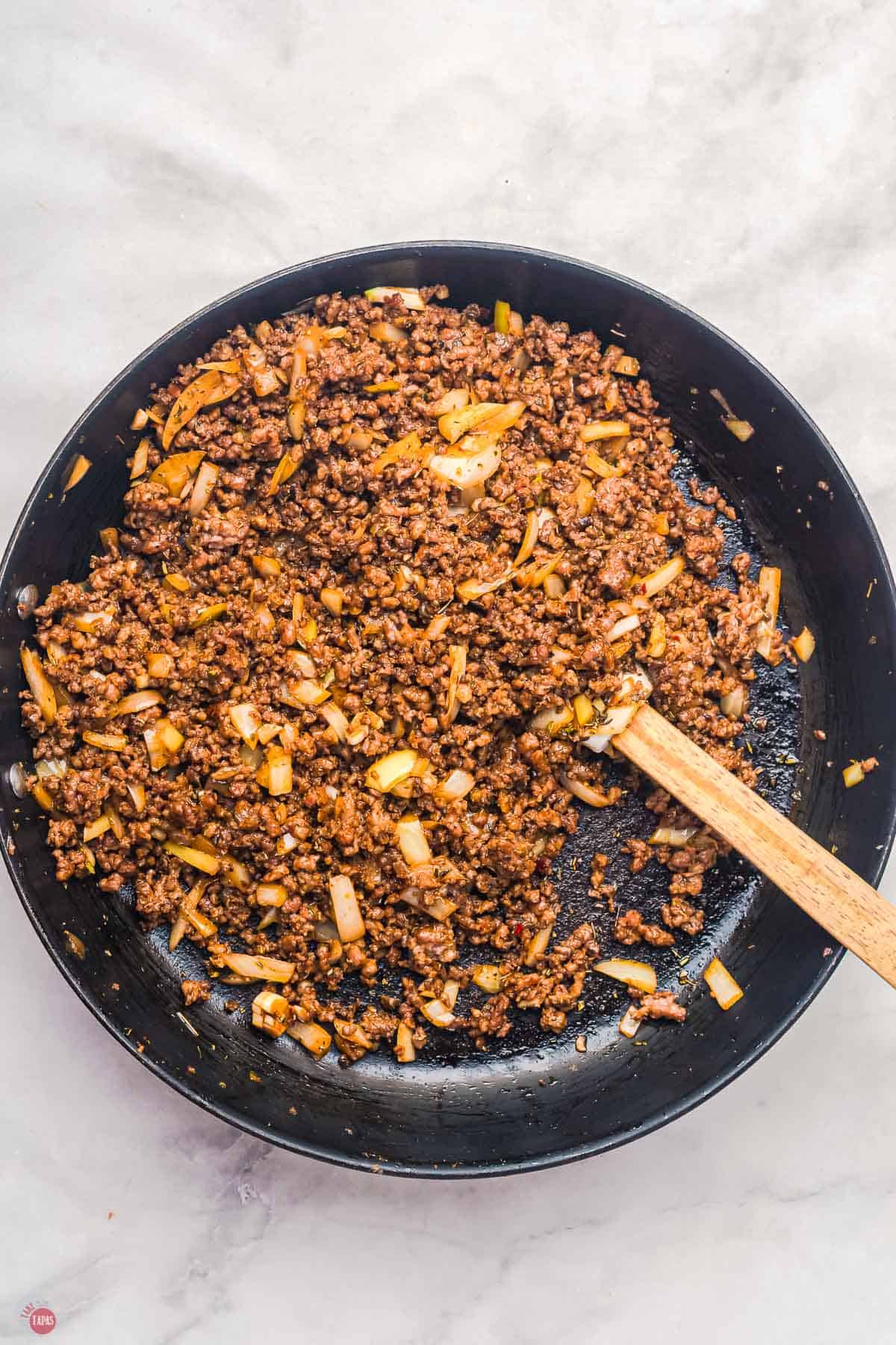 cooked ground beef in a skillet with a wood spoon