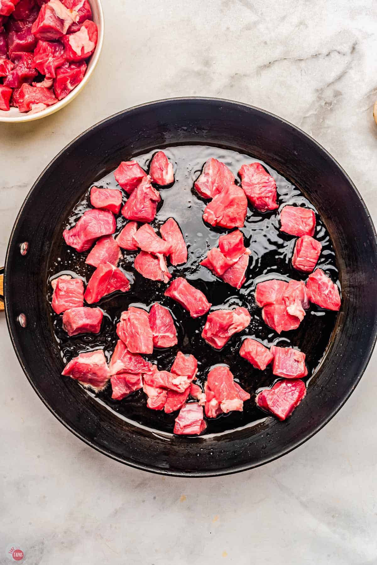 cubes of steak searing in a cast iron skillet
