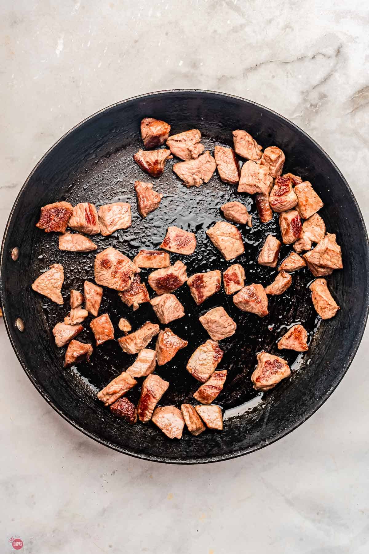 sirloin steak cubes in a skillet on a marble counter