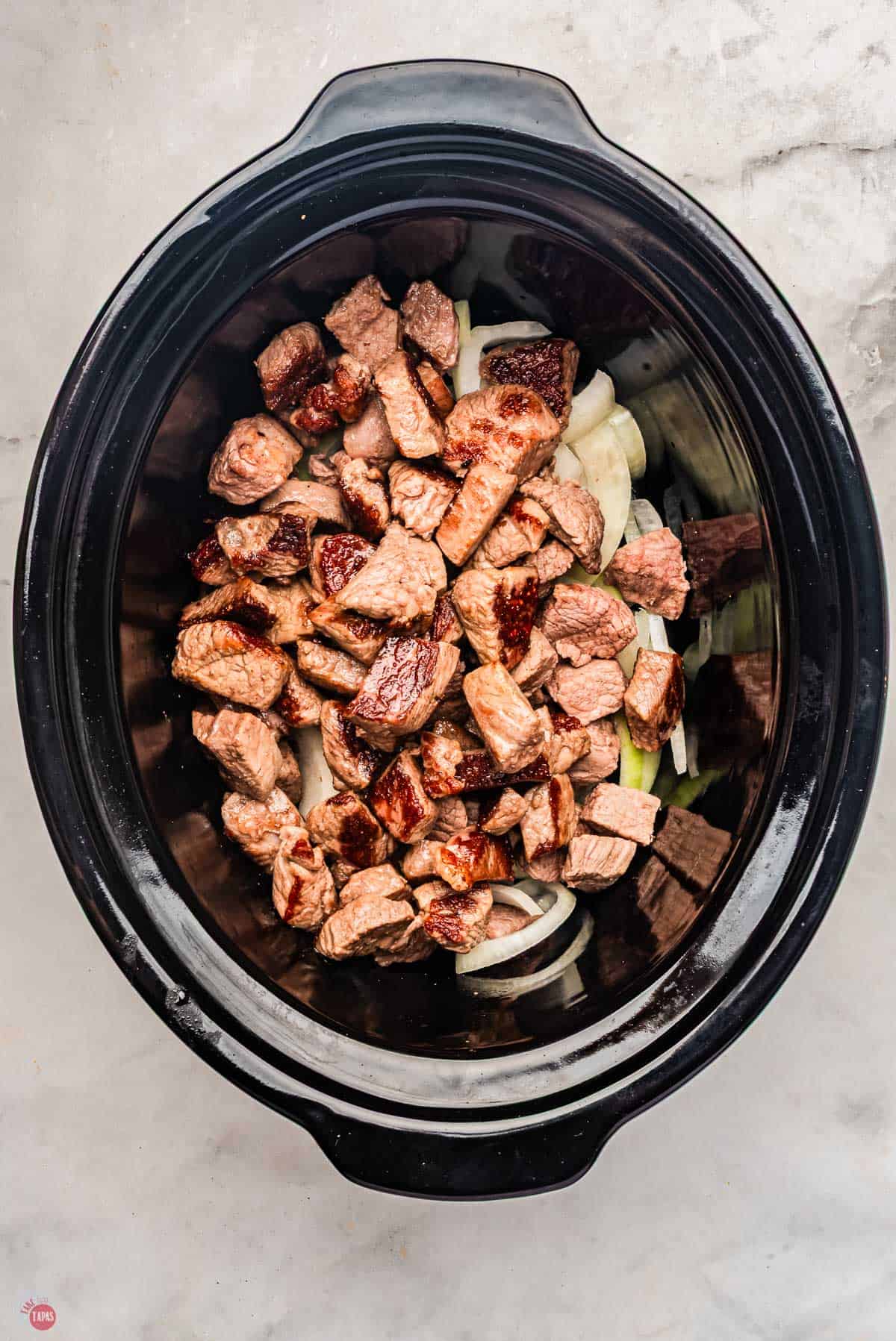 slow cooker bowl with sliced onions and pieces of steak on top