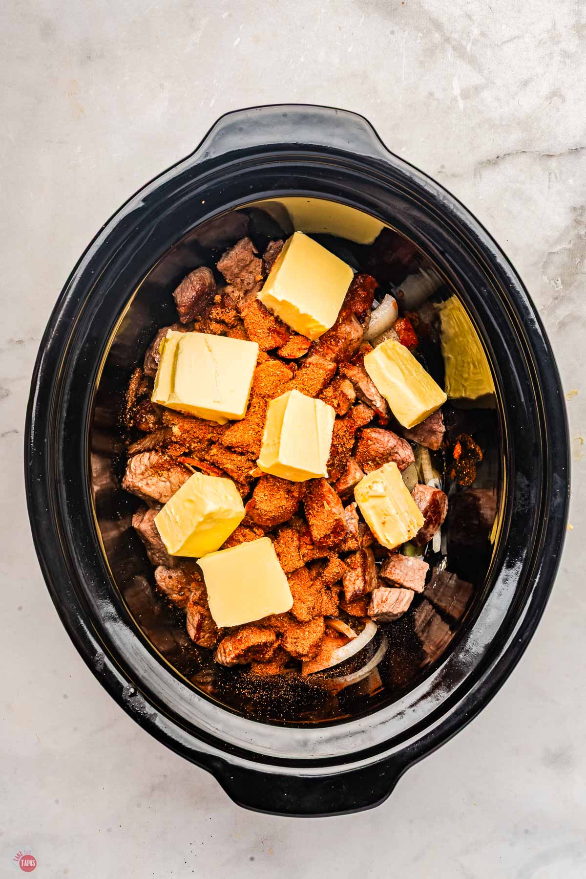 A slow cooker filled with meat and pats of butter