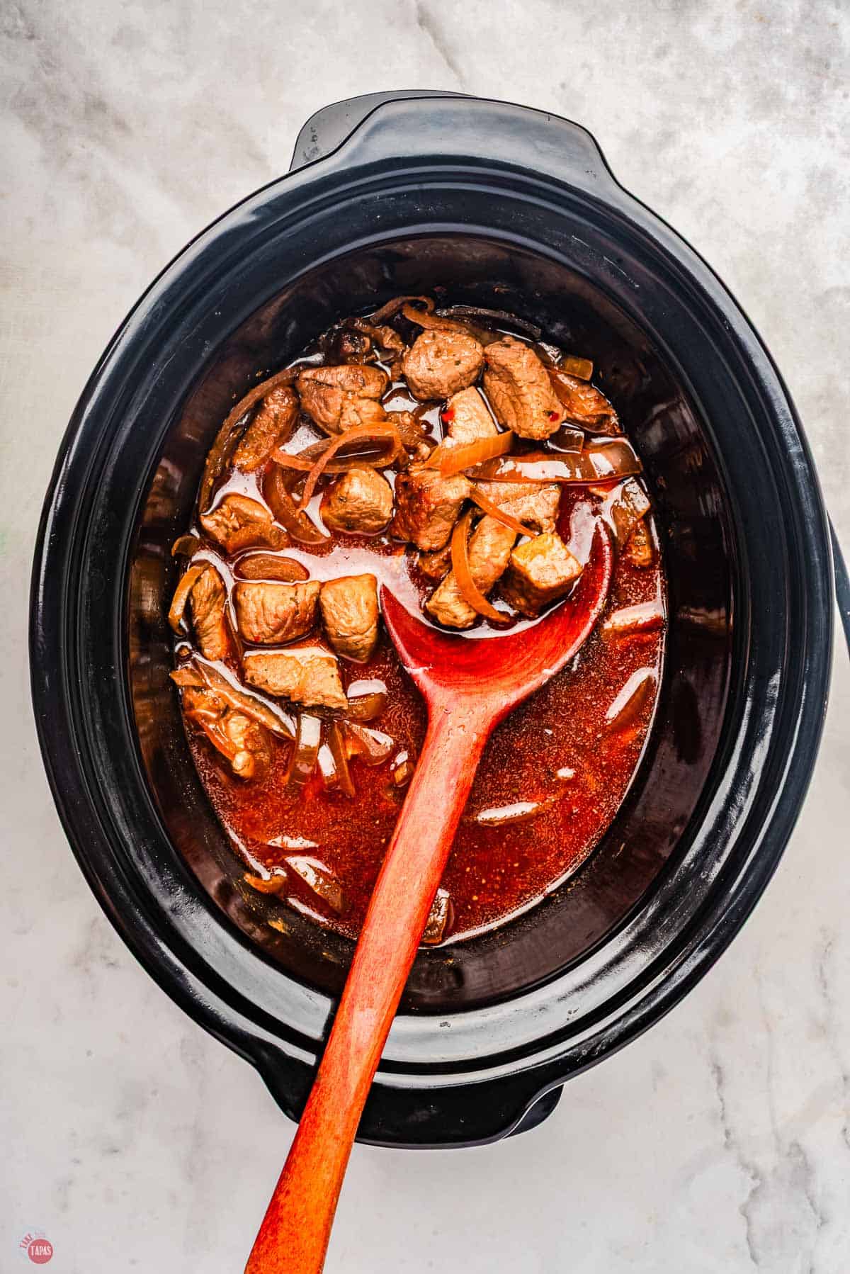 Slow cooker with cubes of steak and broth in it