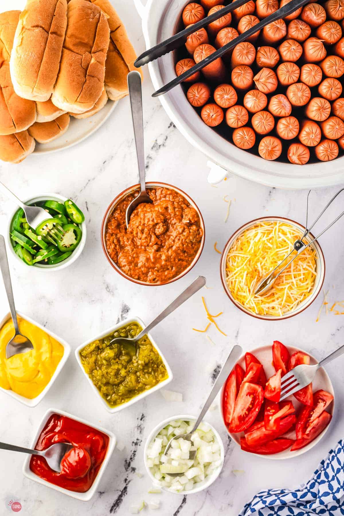 ingredients for hot dogs in individual bowls with spoons in them