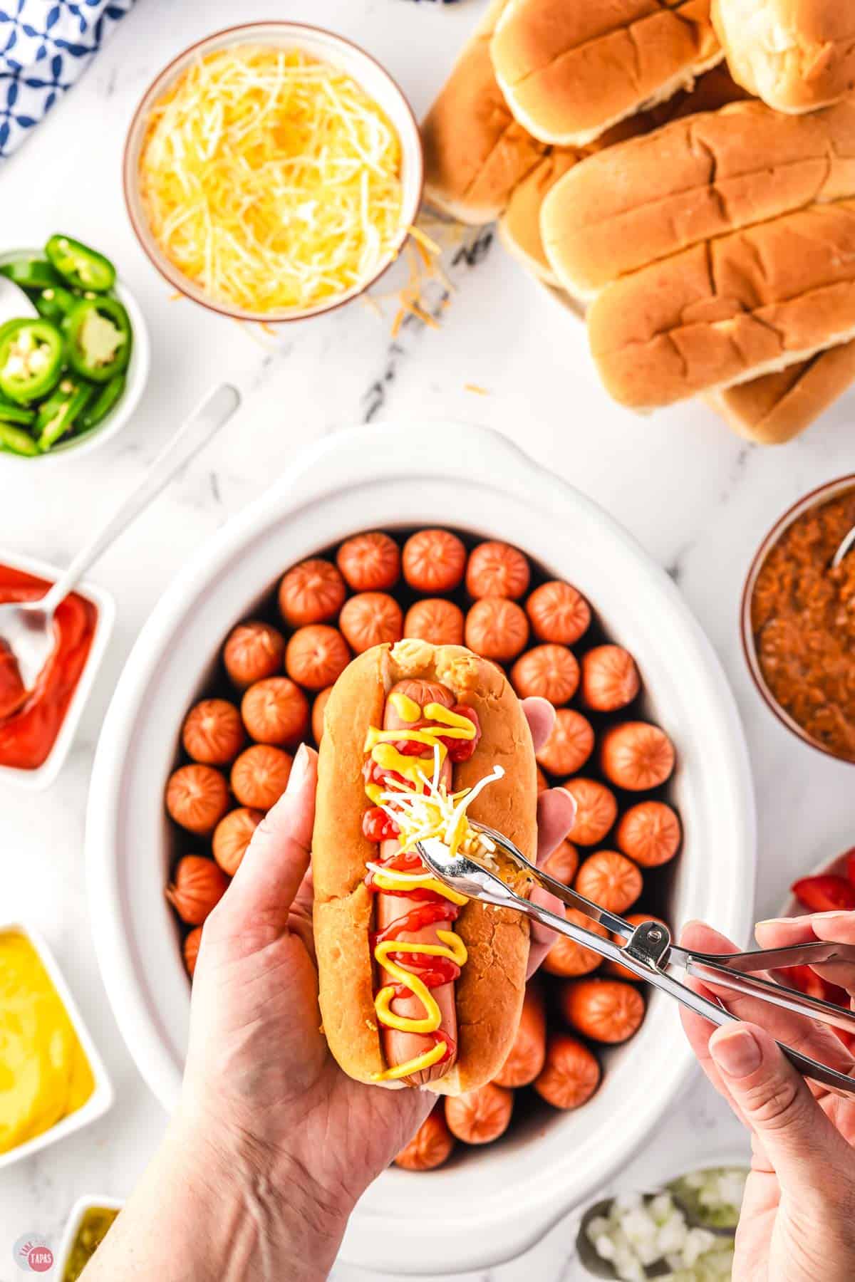 hand holding a hot dog over a crockpot